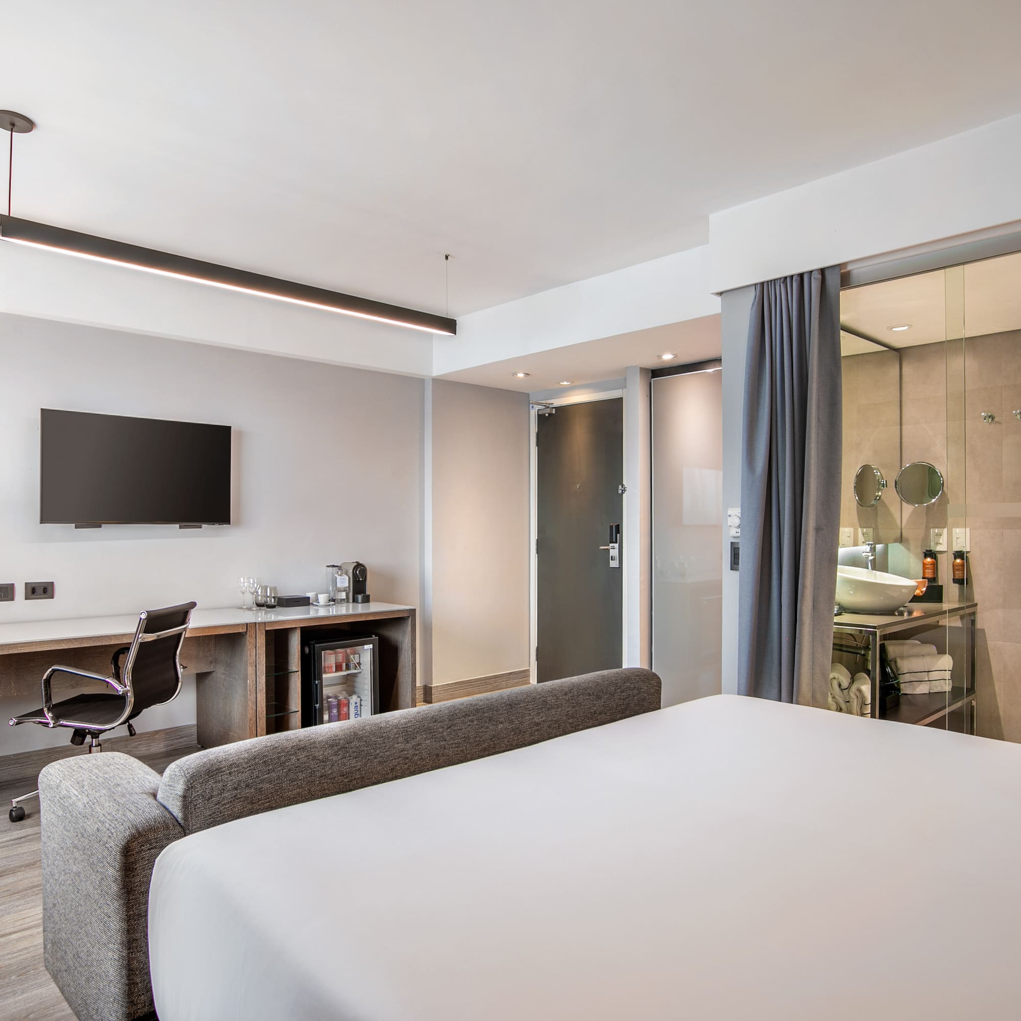 Quarto de hotel moderno com cama, escrivaninha, TV e banheiro de vidro. - Grand Premium - Meliá Ibirapuera, São Paulo