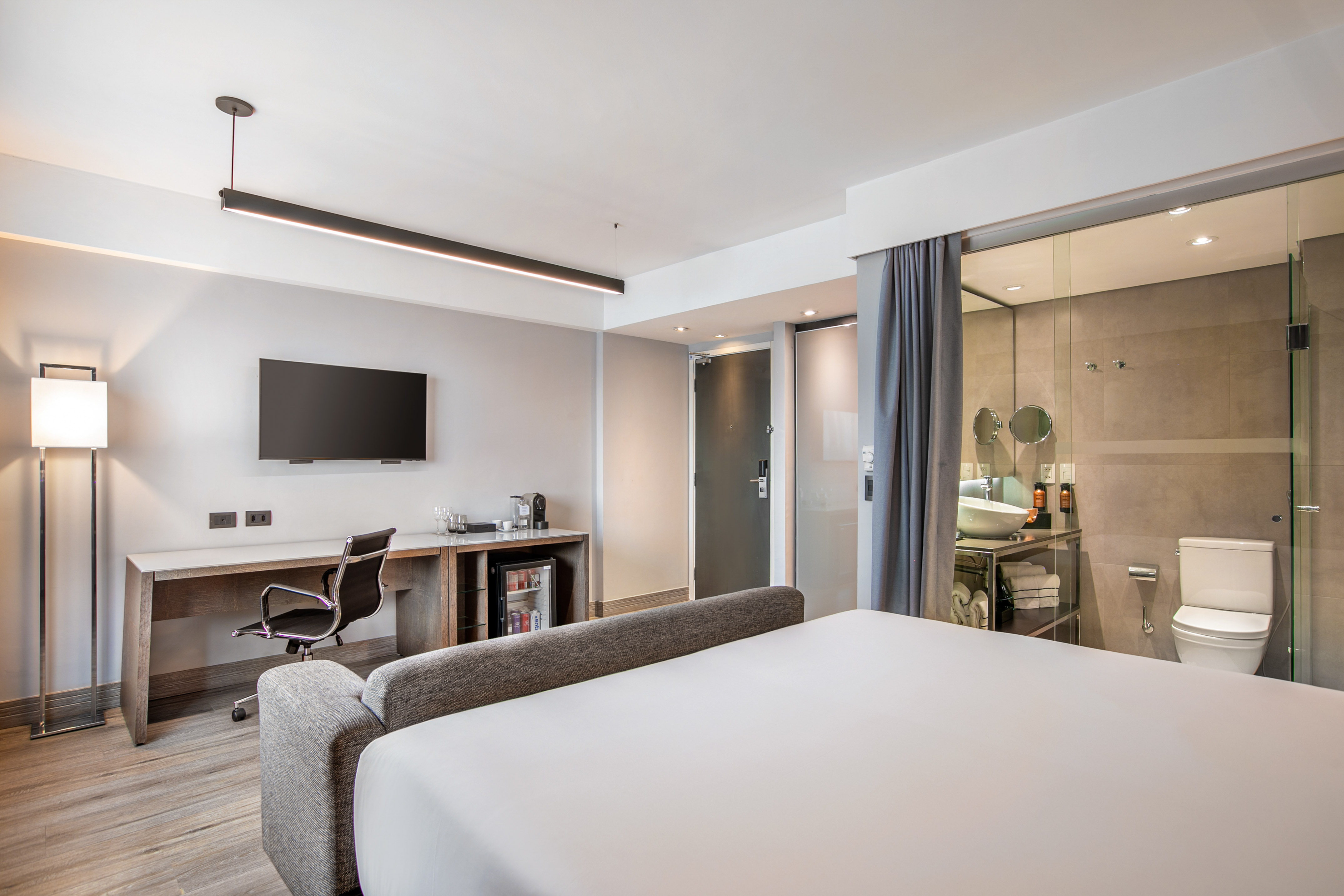 Quarto de hotel moderno com cama, escrivaninha, TV e banheiro de vidro. - Grand Premium - Meliá Ibirapuera, São Paulo