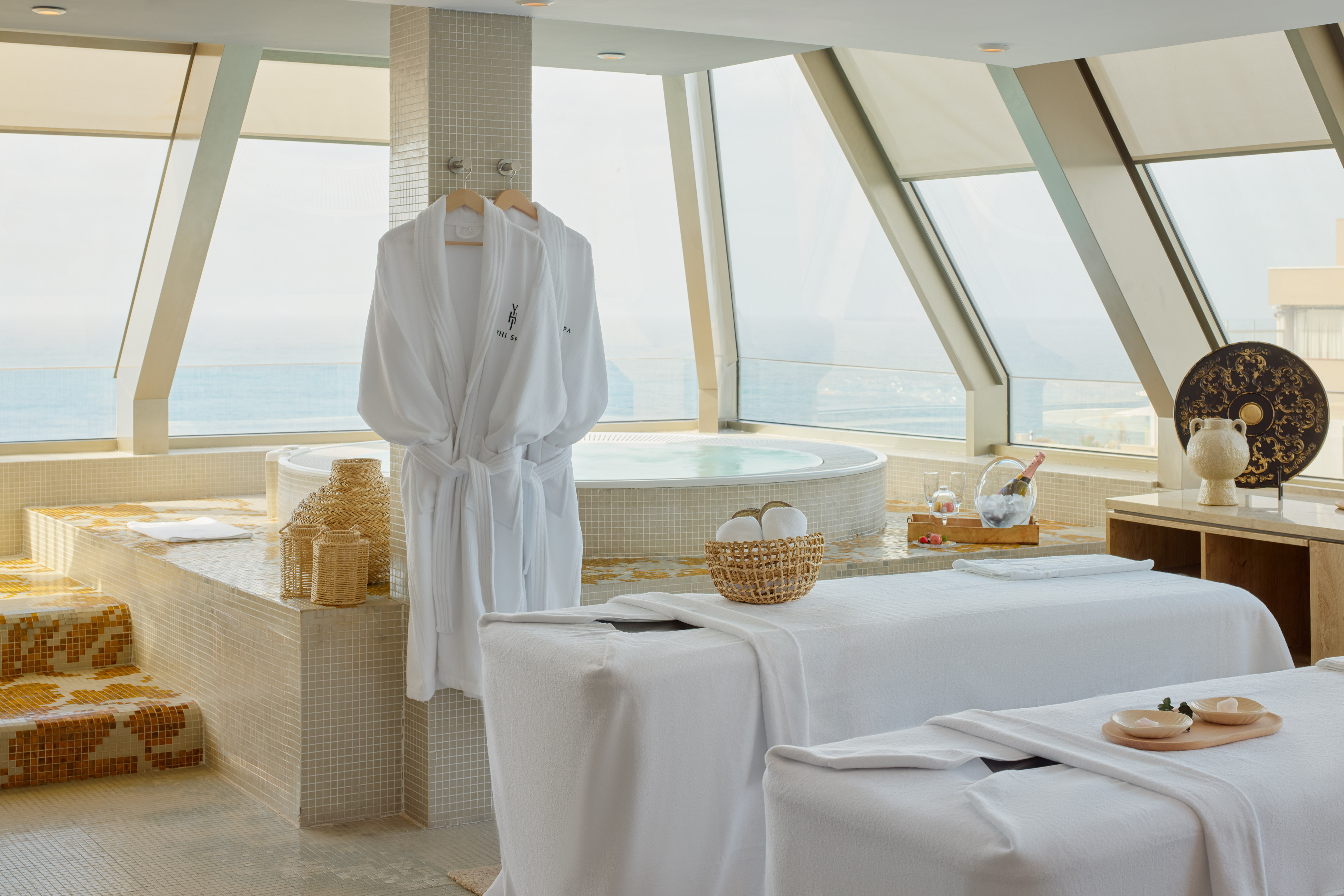 Luxury spa suite with ocean view, massage tables, hot tub, and bathrobes.