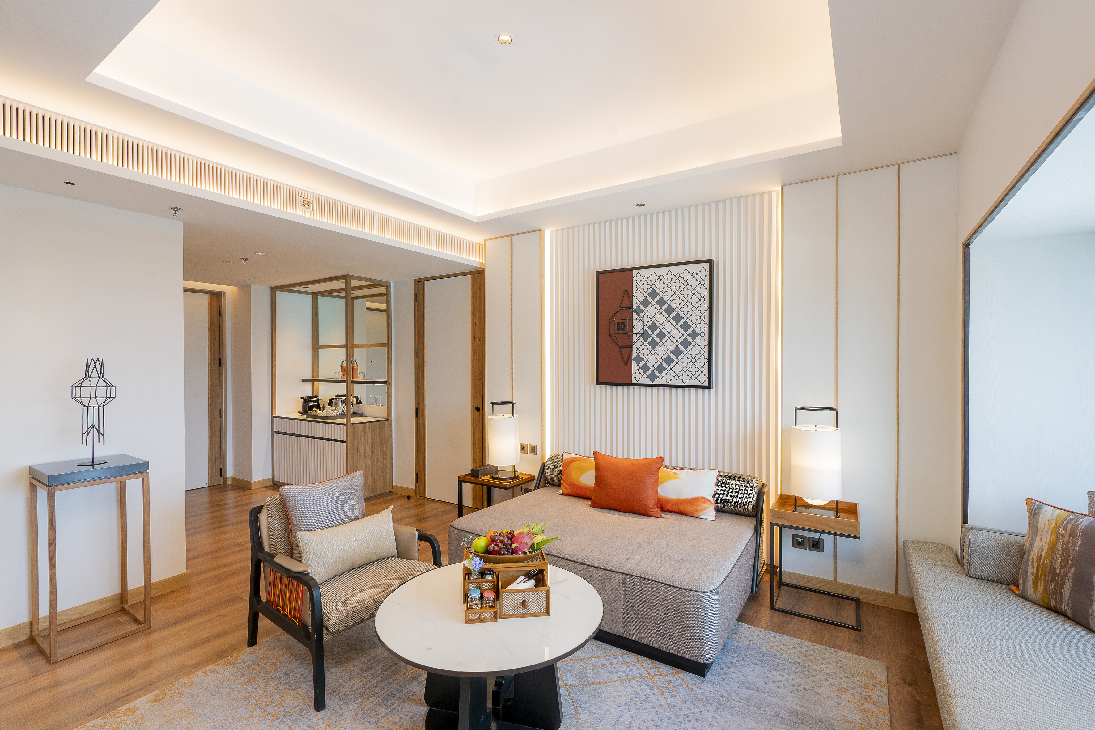 Modern hotel suite with daybed, armchair, coffee table, and mini-bar.