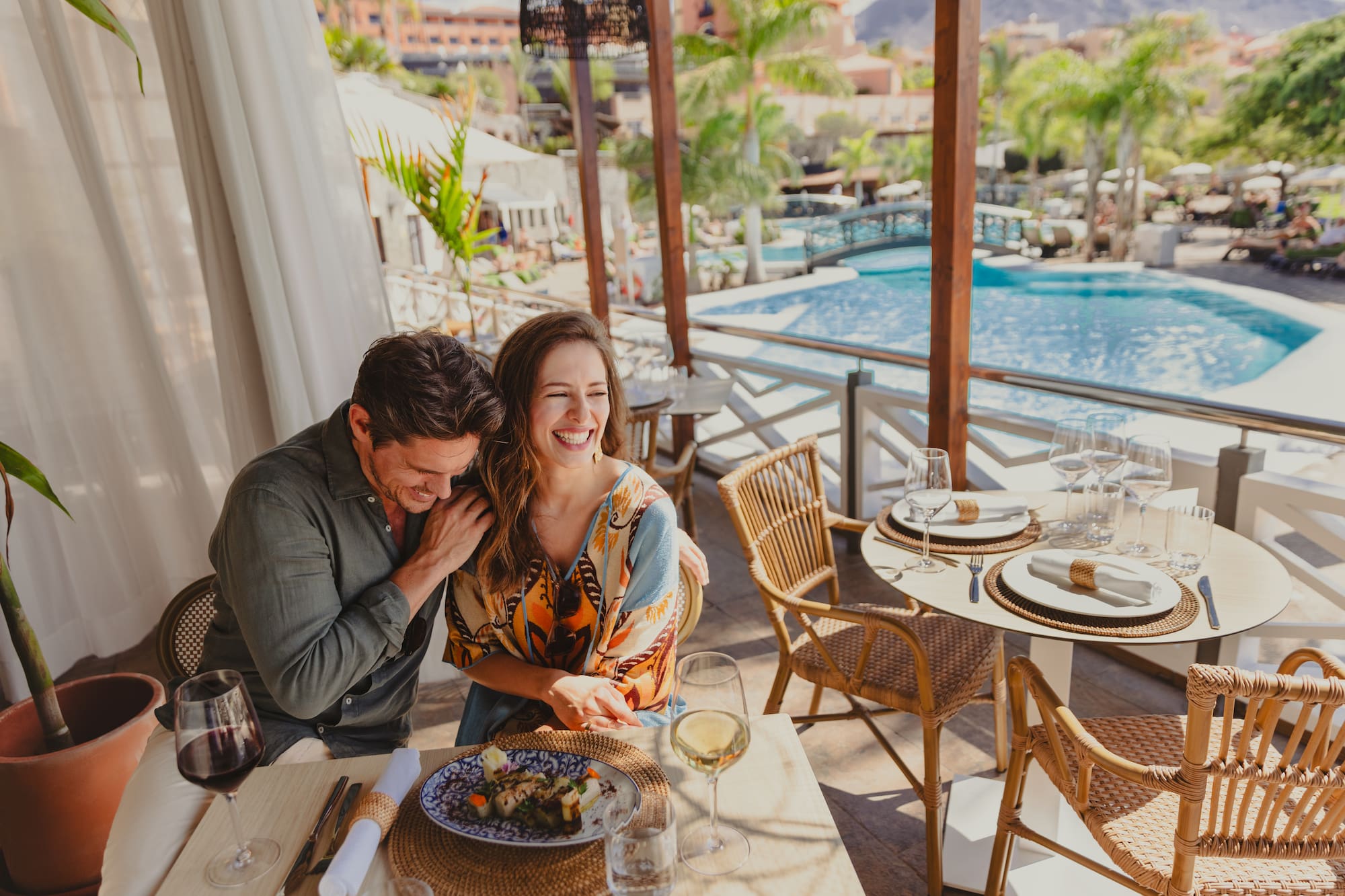 Happy couple dining at an outdoor resort restaurant overlooking a beautiful pool.