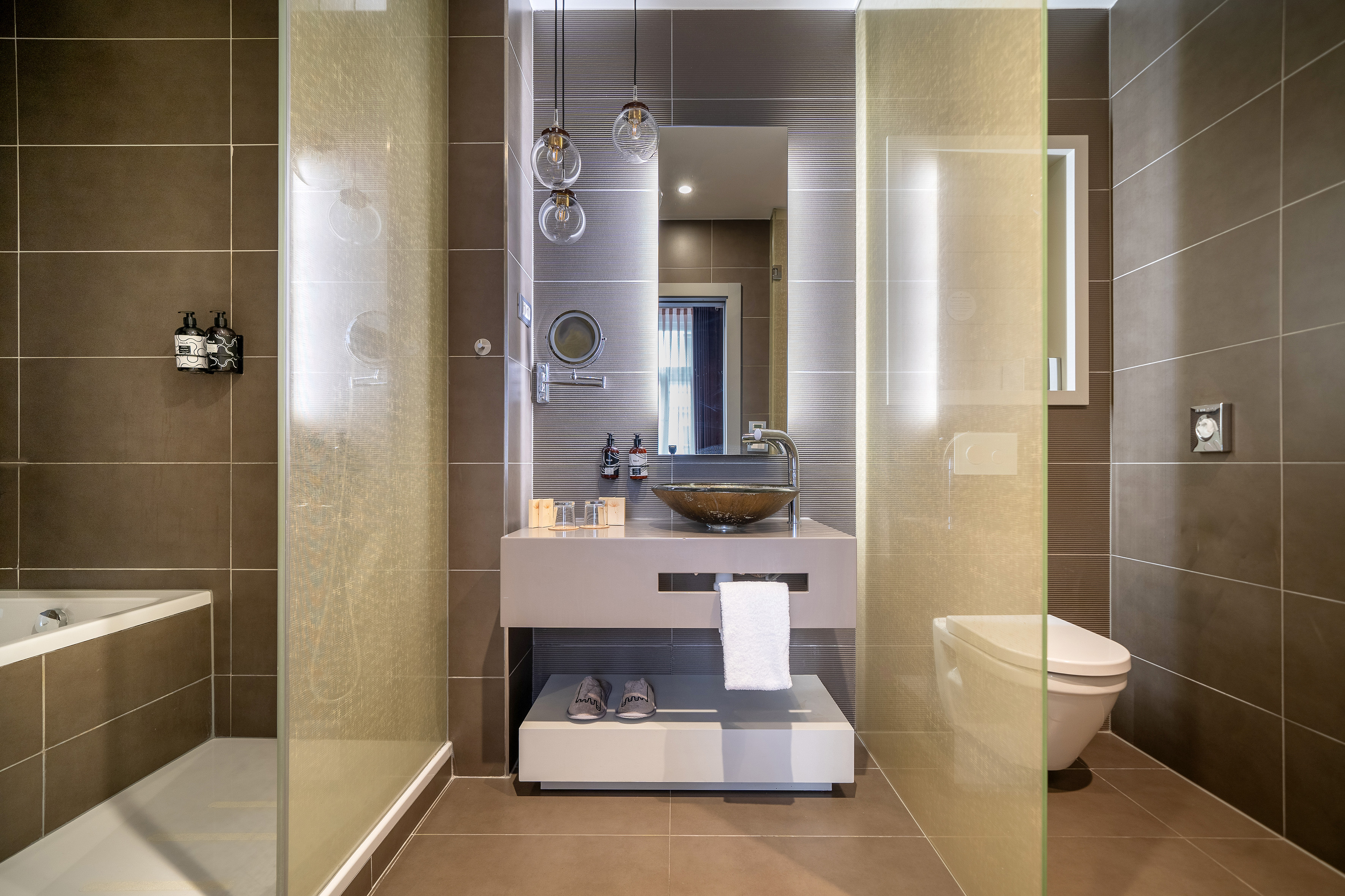 Modern brown bathroom with vanity, vessel sink, glass shower, and toilet.