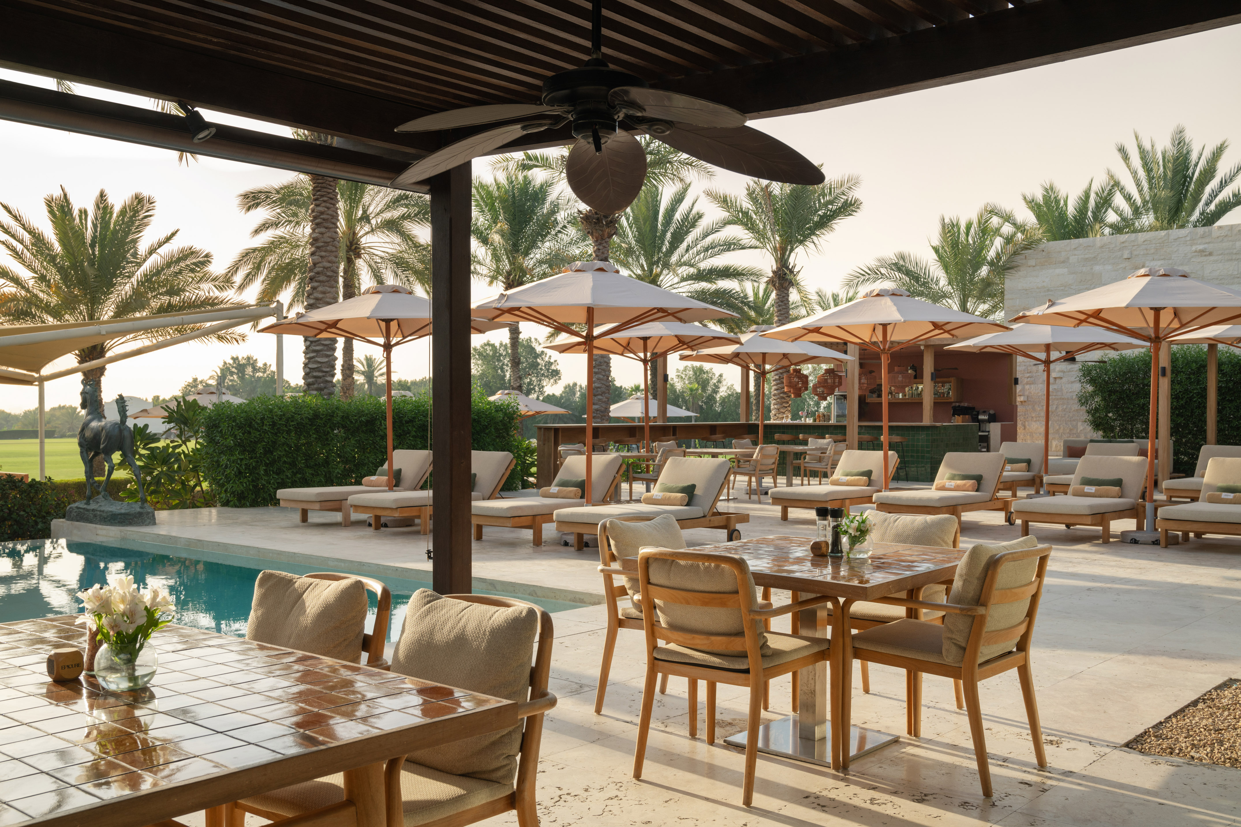 Luxury resort outdoor dining patio with pool, palm trees, sun loungers, and bar.
