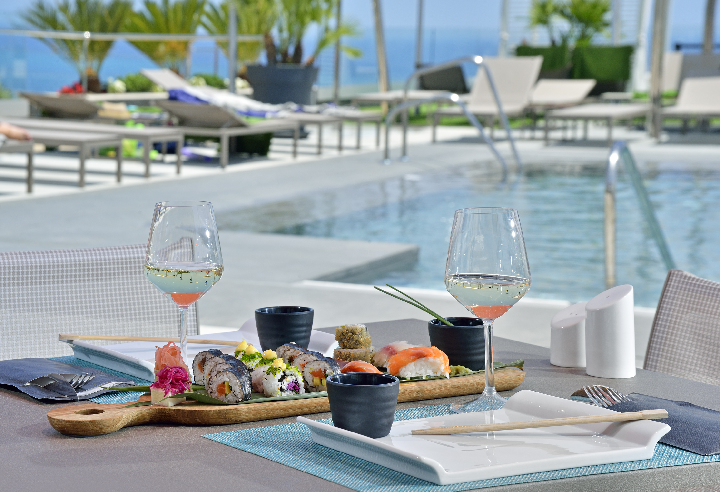 Sushi and wine by a luxury resort pool with ocean view.