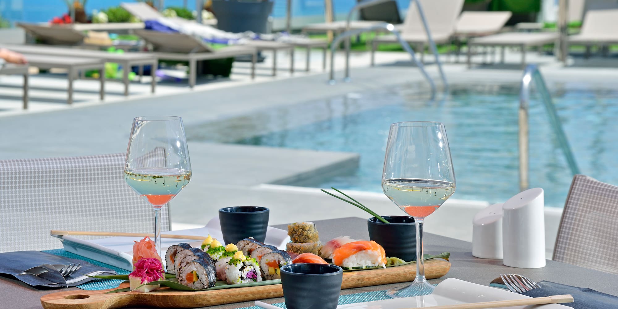 Sushi platter and white wine by a resort pool overlooking the ocean.