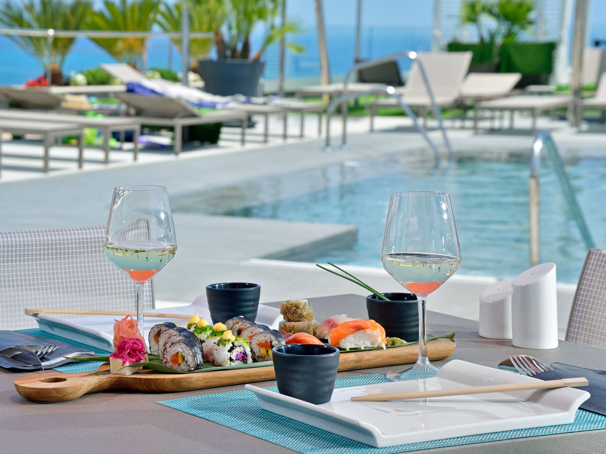Sushi and wine by a luxury resort pool with ocean view.
