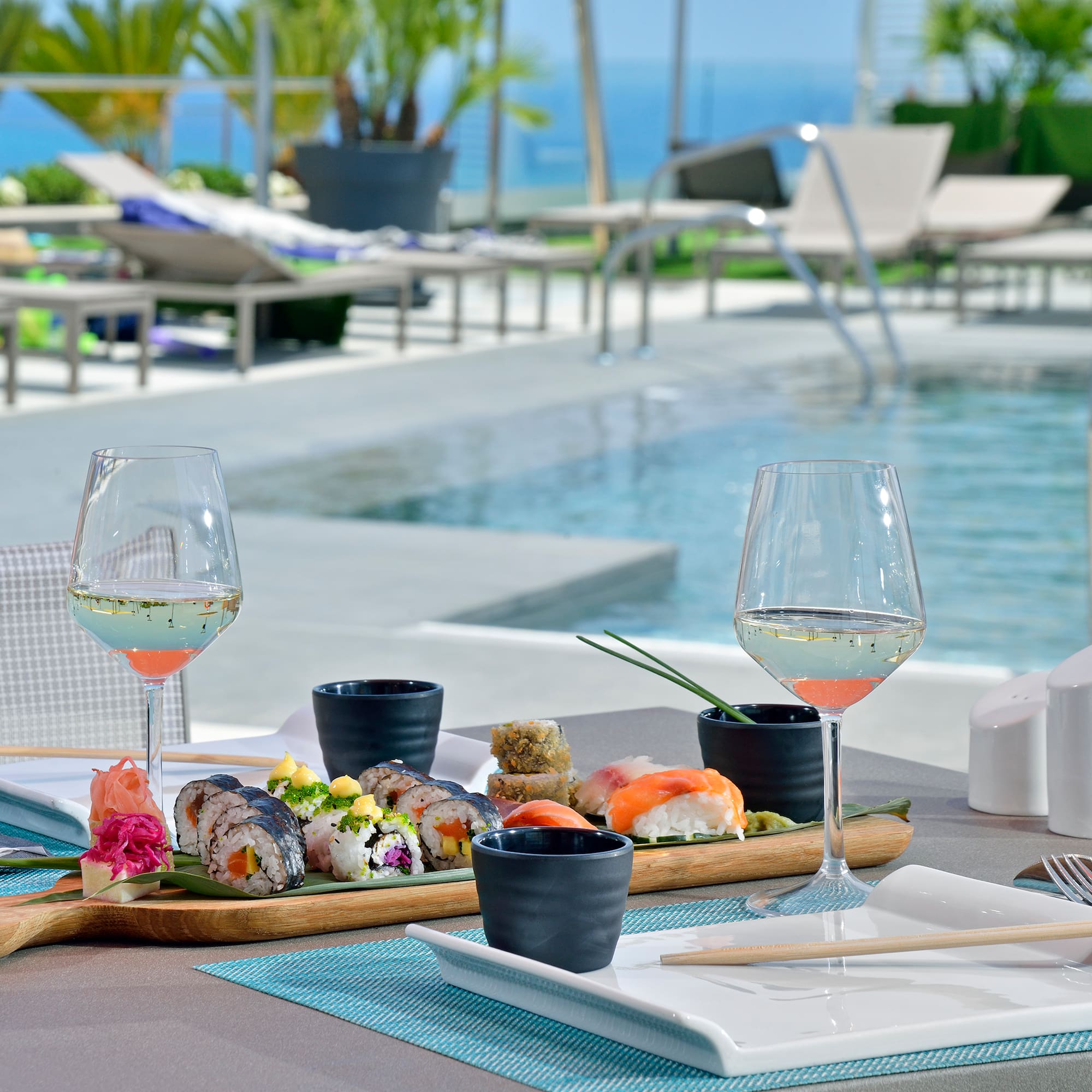 Sushi platter and white wine by a resort pool overlooking the ocean.