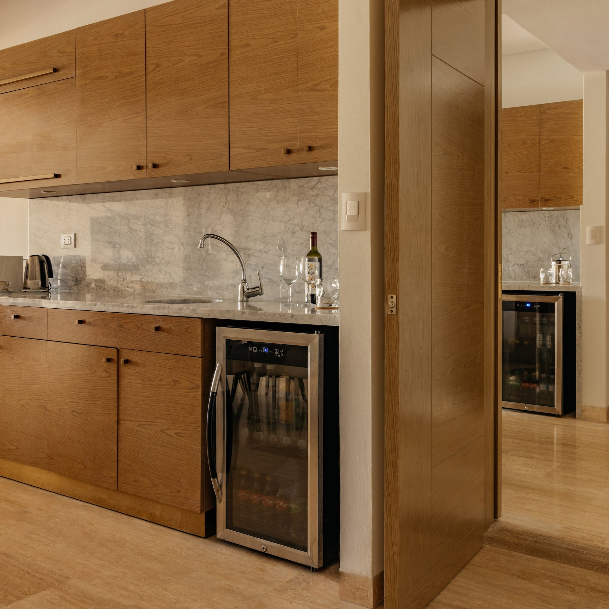 Hotel kitchenette with wood cabinets, marble counter, sink, and beverage cooler.