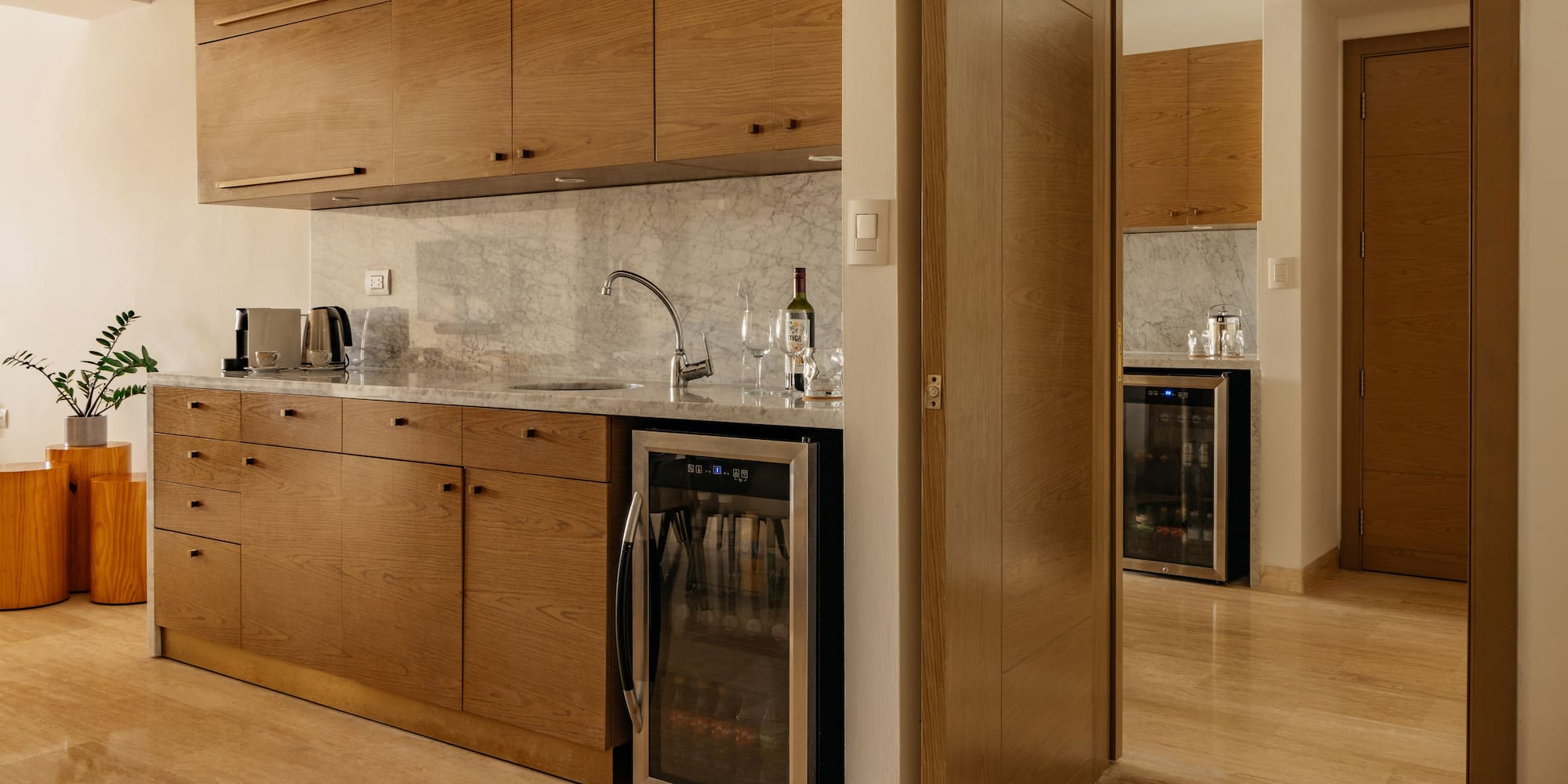 Modern kitchenette with oak cabinets, marble counter, sink, and beverage fridge.