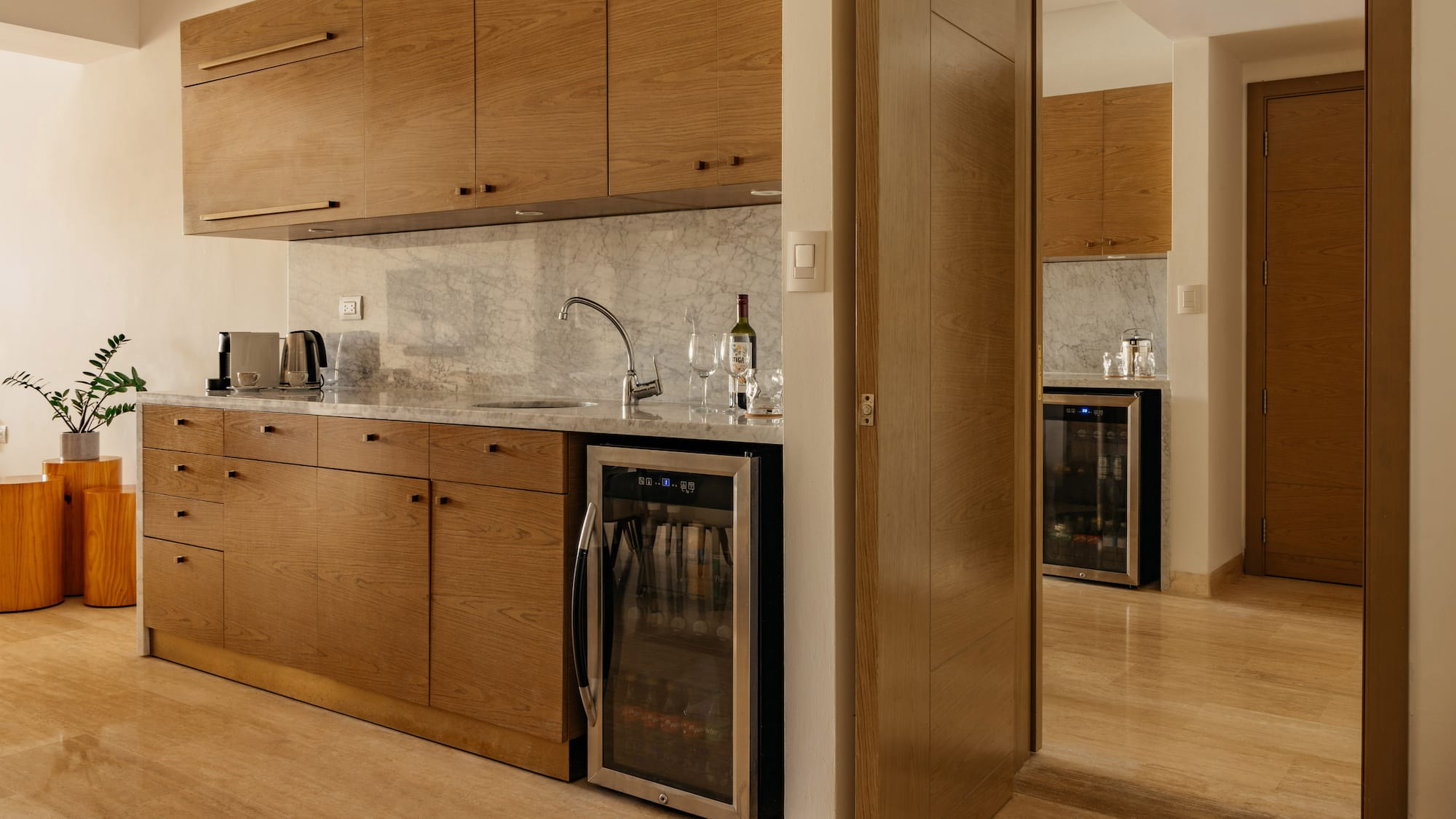 Modern kitchenette with oak cabinets, marble counter, sink, and beverage fridge.