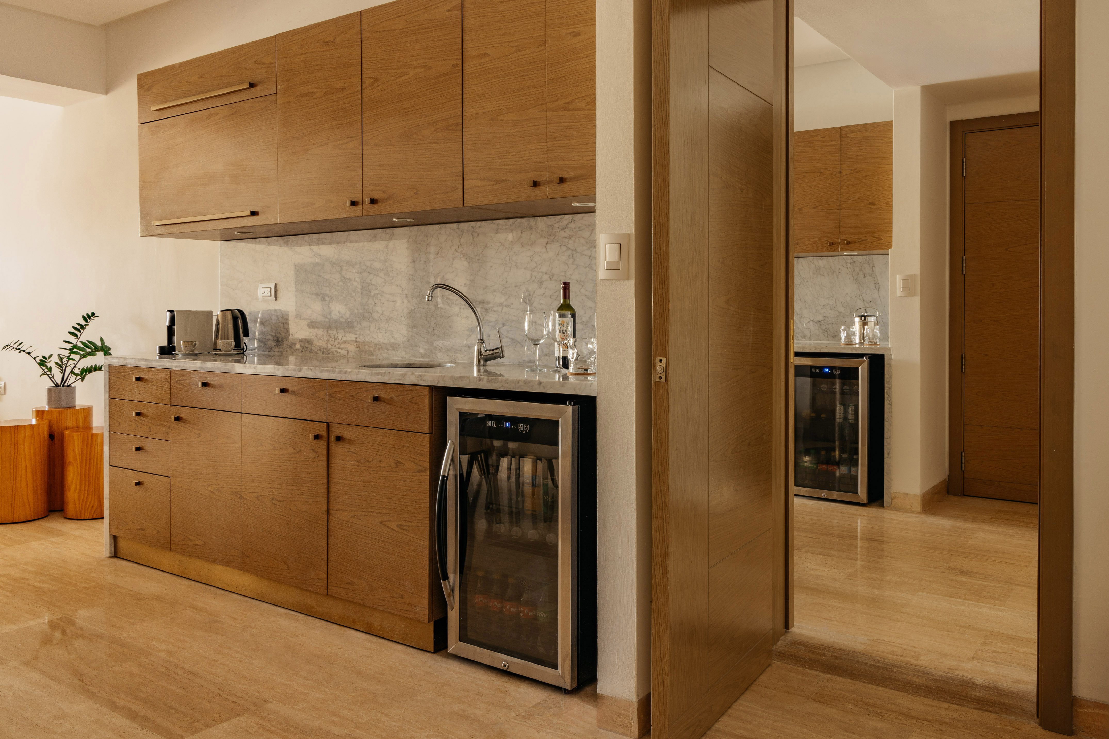 Modern kitchenette with oak cabinets, marble counter, sink, and beverage fridge.