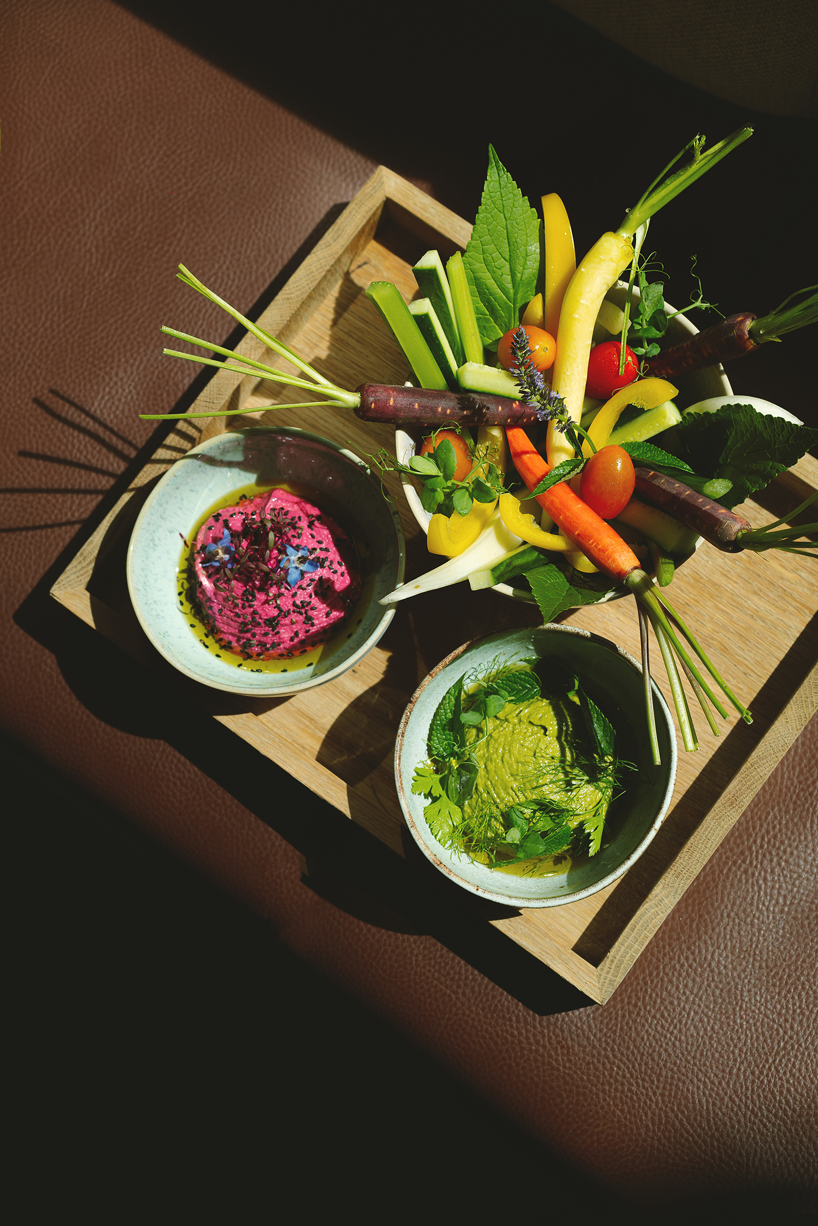 Colorful crudités platter with beet and herb dips on a wooden tray.
