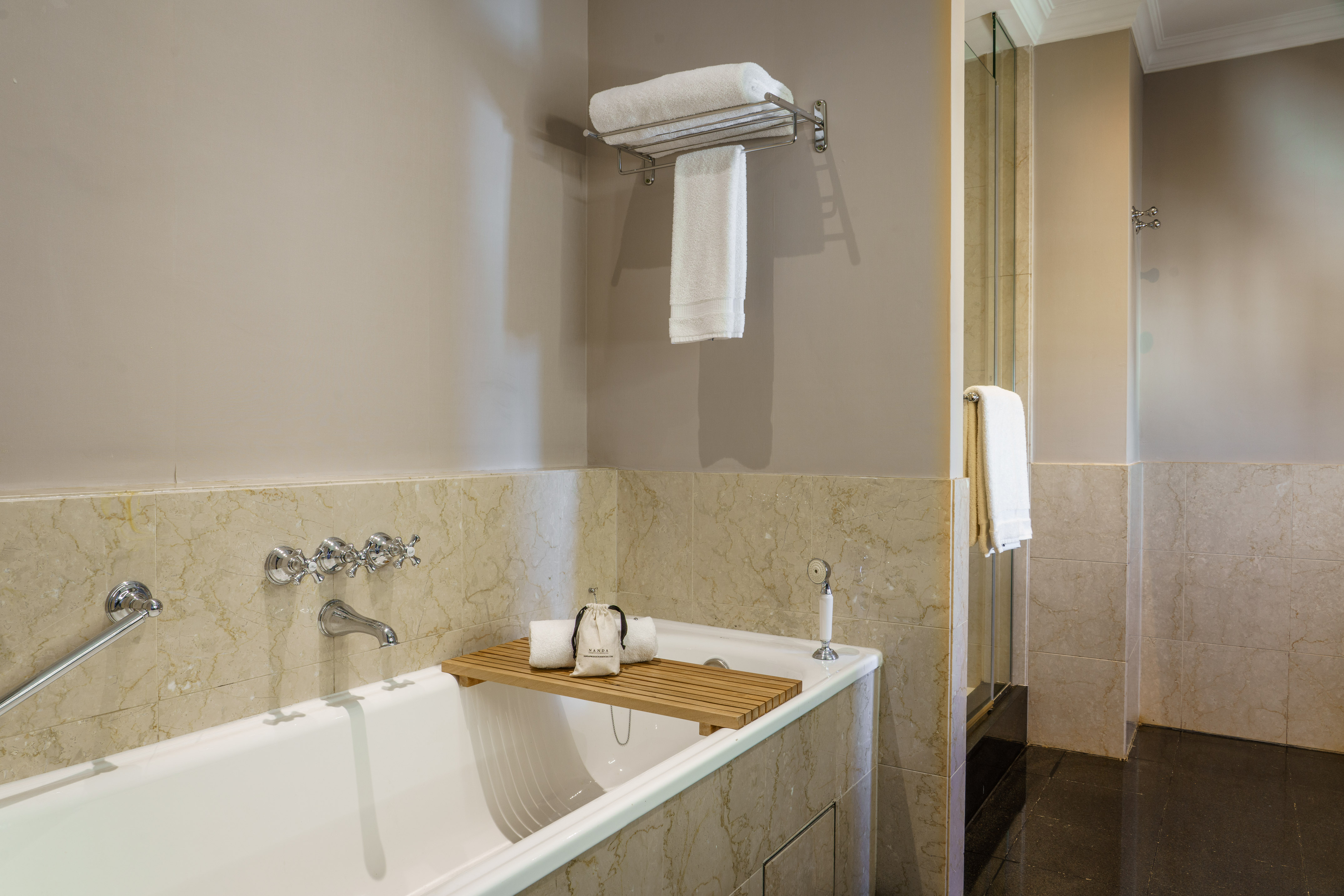 Bathroom with white bathtub, marble walls, fresh towels, and glass shower.