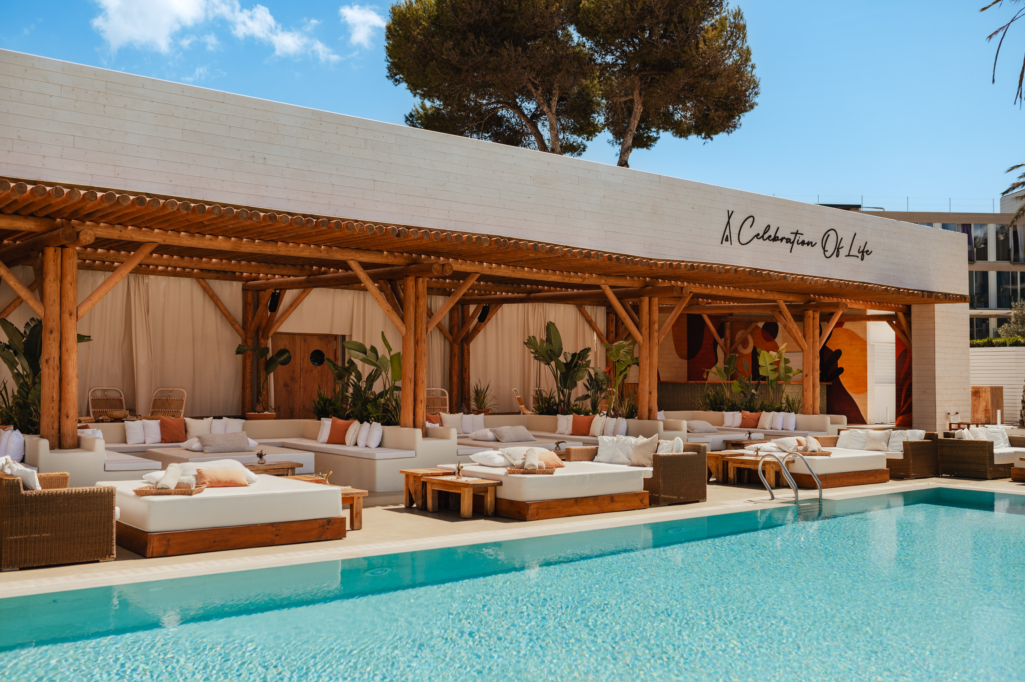 Luxury resort pool lounge with daybeds, wooden pergola, and blue pool.