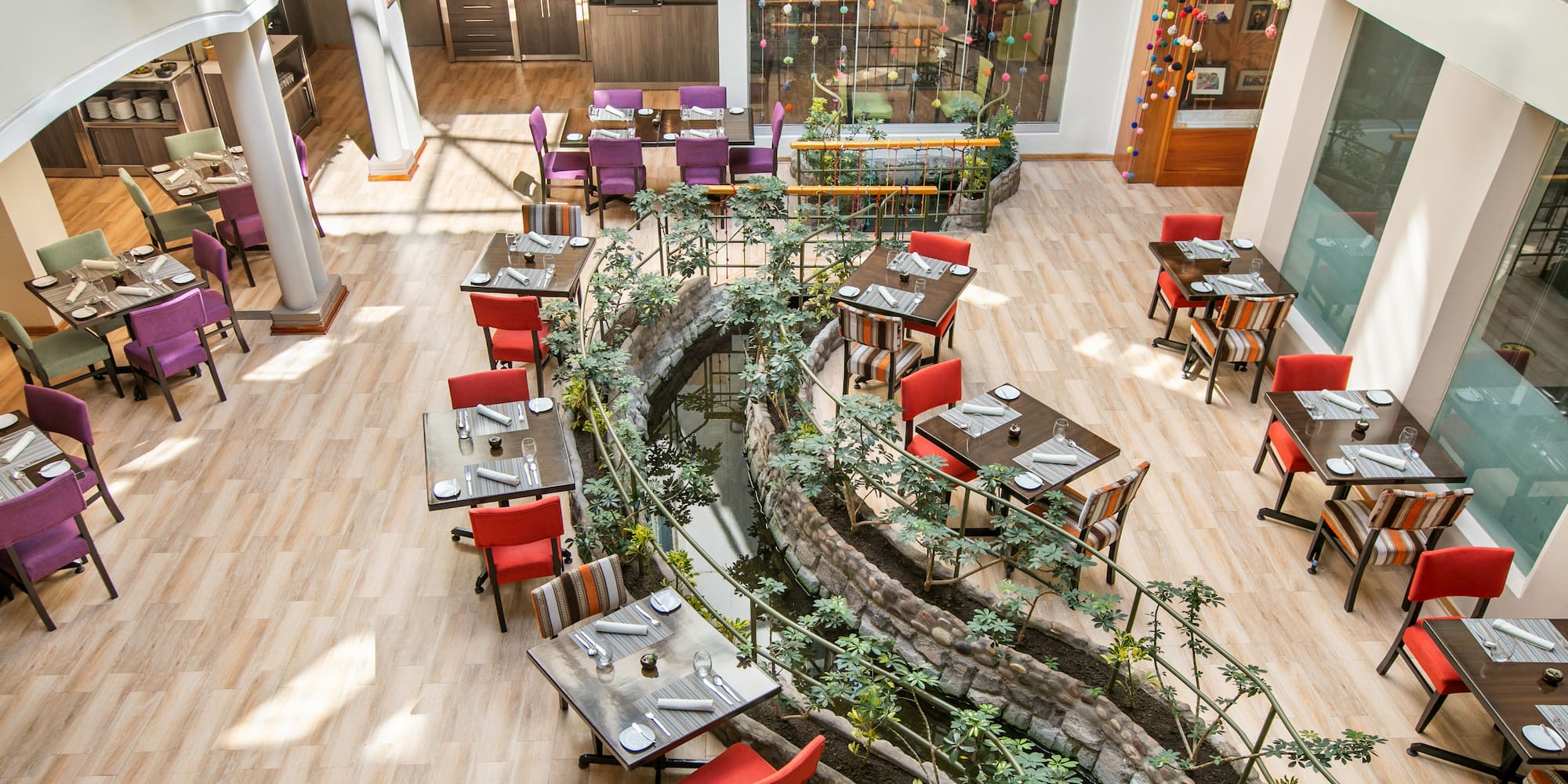 Vibrant restaurant interior with set dining tables, colorful chairs, and winding stream.