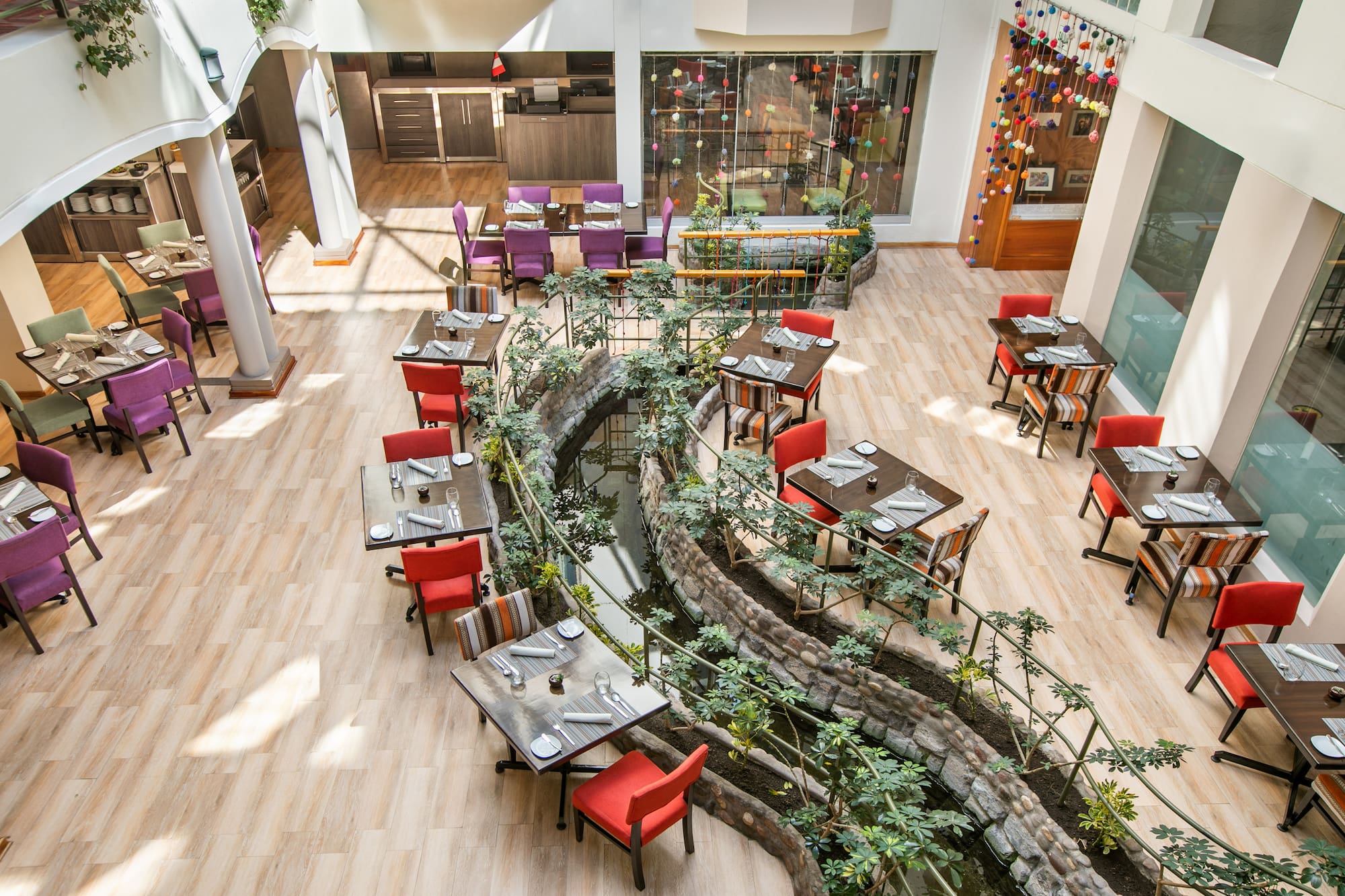 Vibrant restaurant interior with set dining tables, colorful chairs, and winding stream. - Hotel Cusco La Paccha Affiliated by Meliá, Cusco