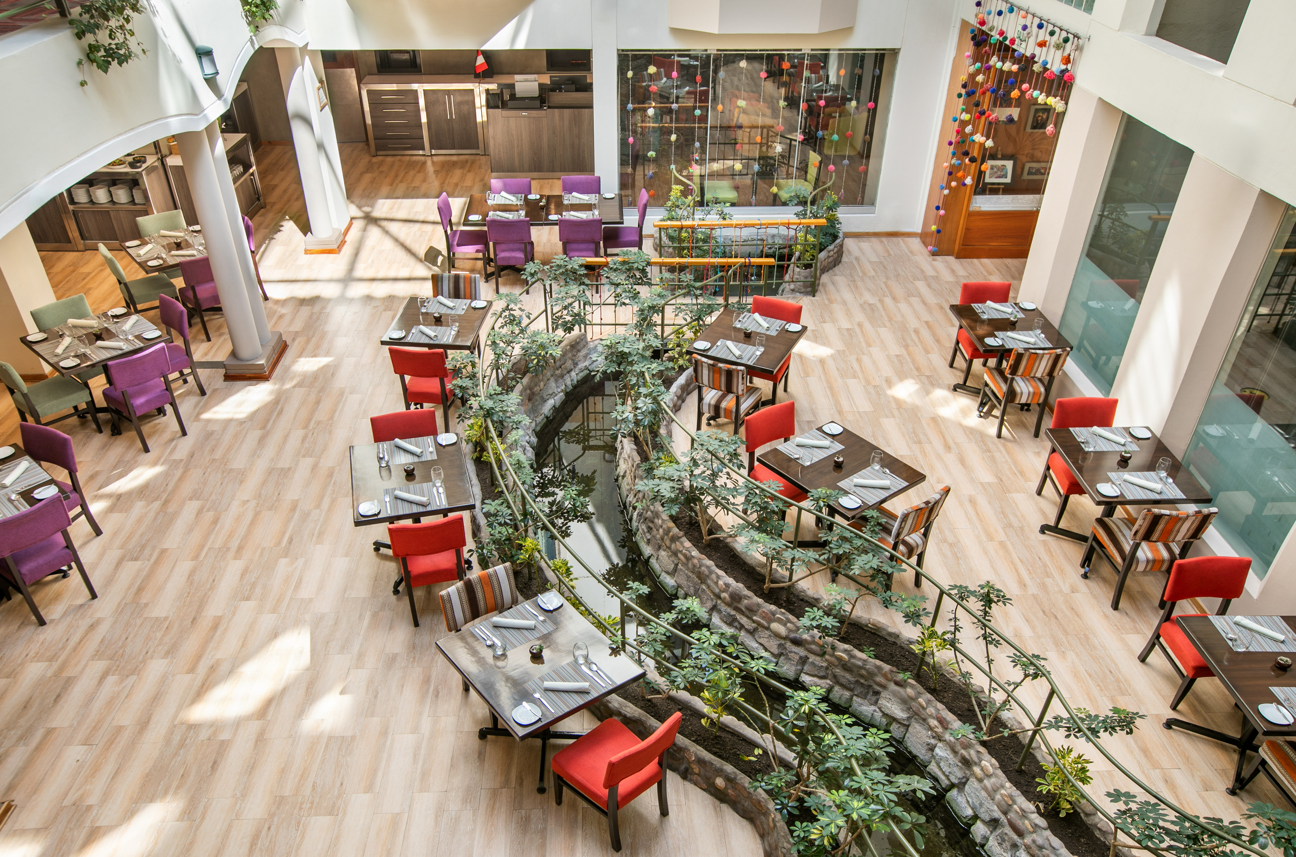 Vibrant restaurant interior with set dining tables, colorful chairs, and winding stream.