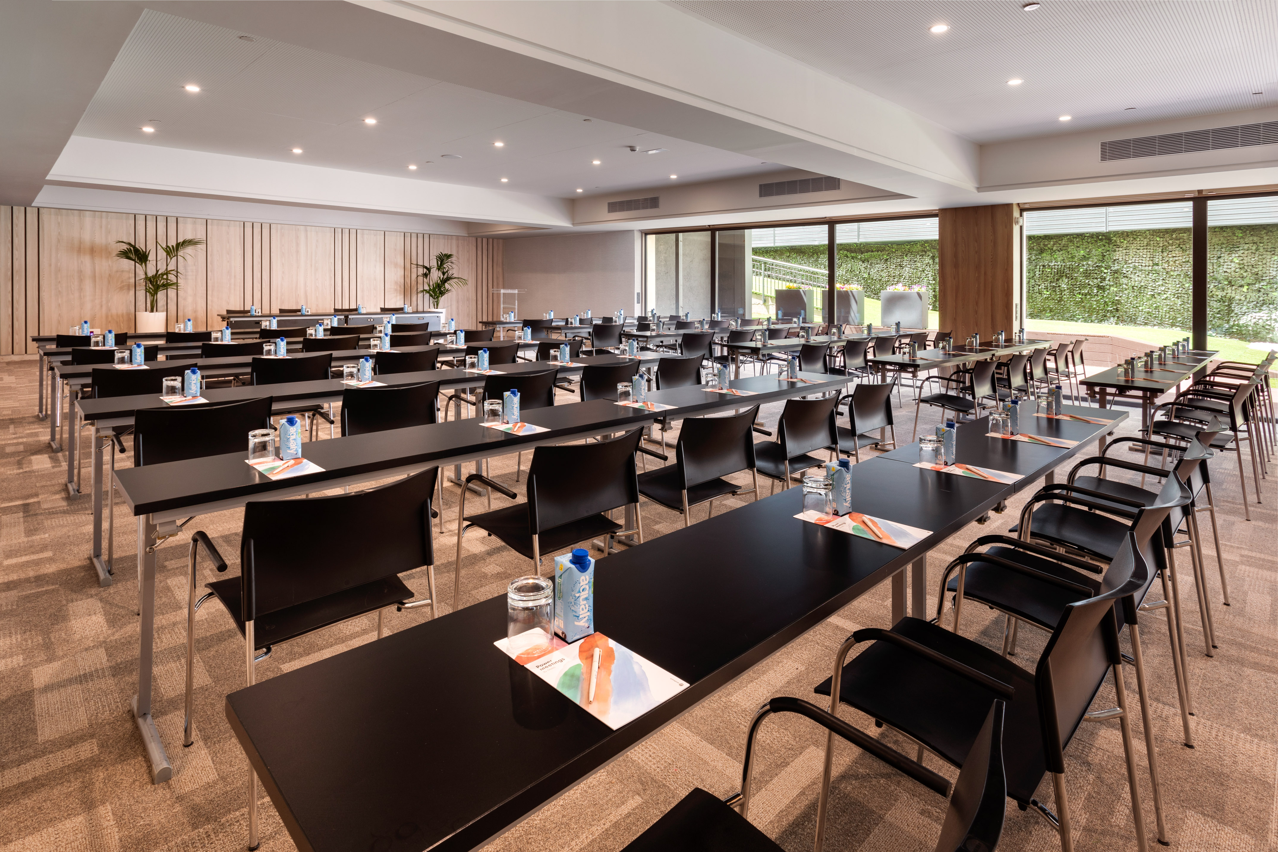 Spacious conference room with tables, chairs, water bottles, and windows.