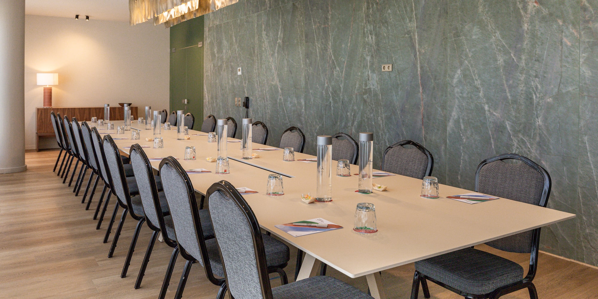 Modern conference room with long table, chairs, and green marble wall.