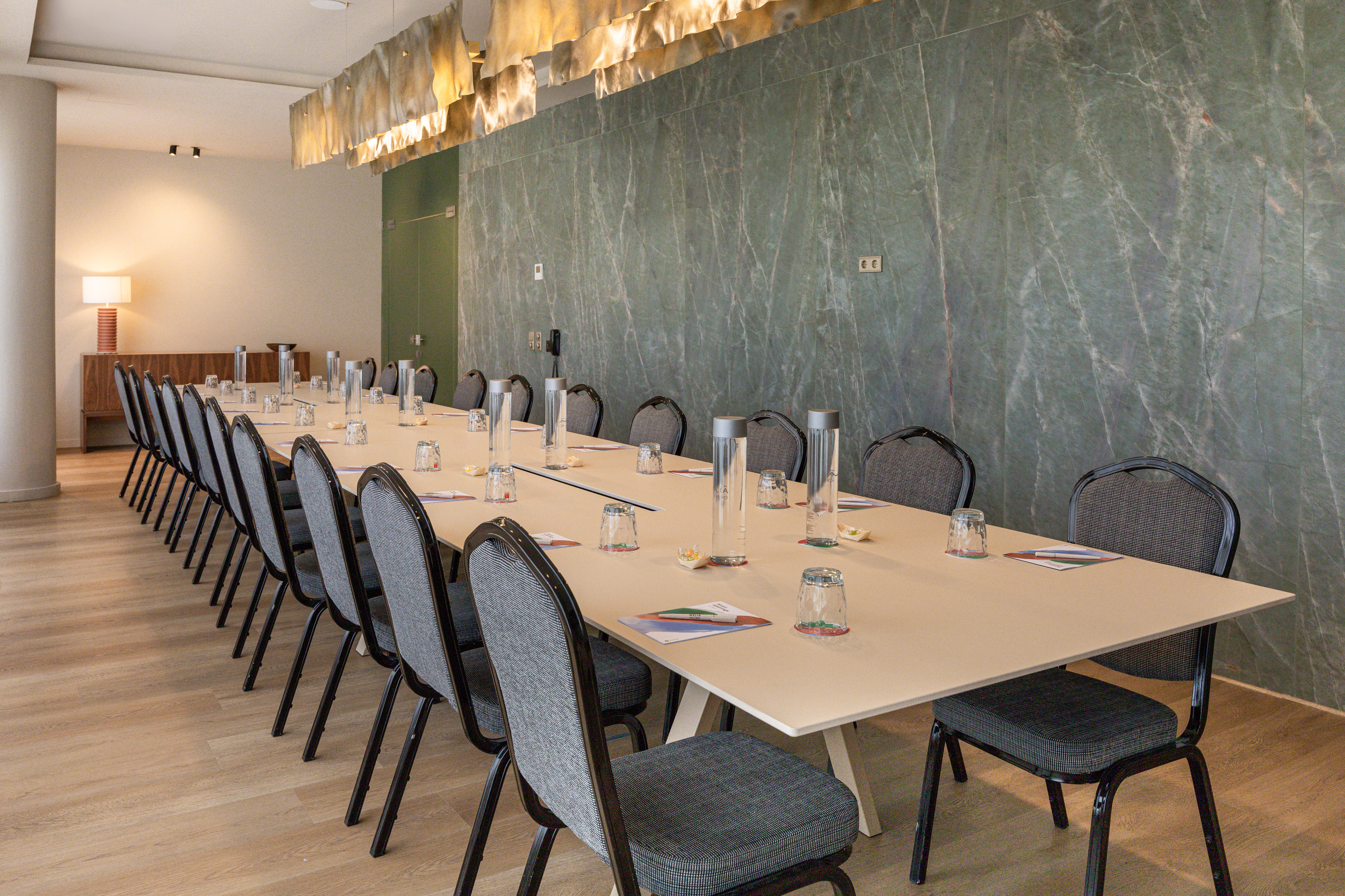 Modern conference room with long table, chairs, and green marble wall.