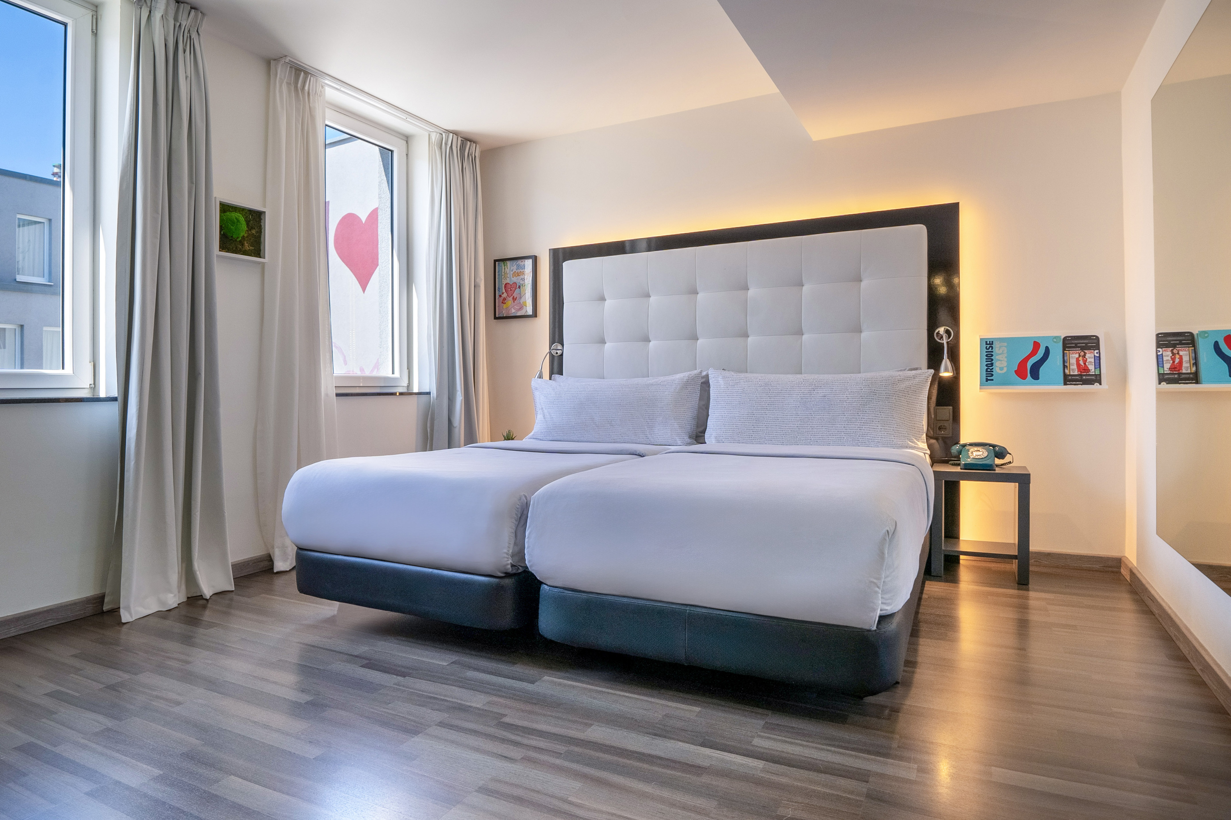 Modern hotel room with twin beds, backlit headboard, and wood floor.