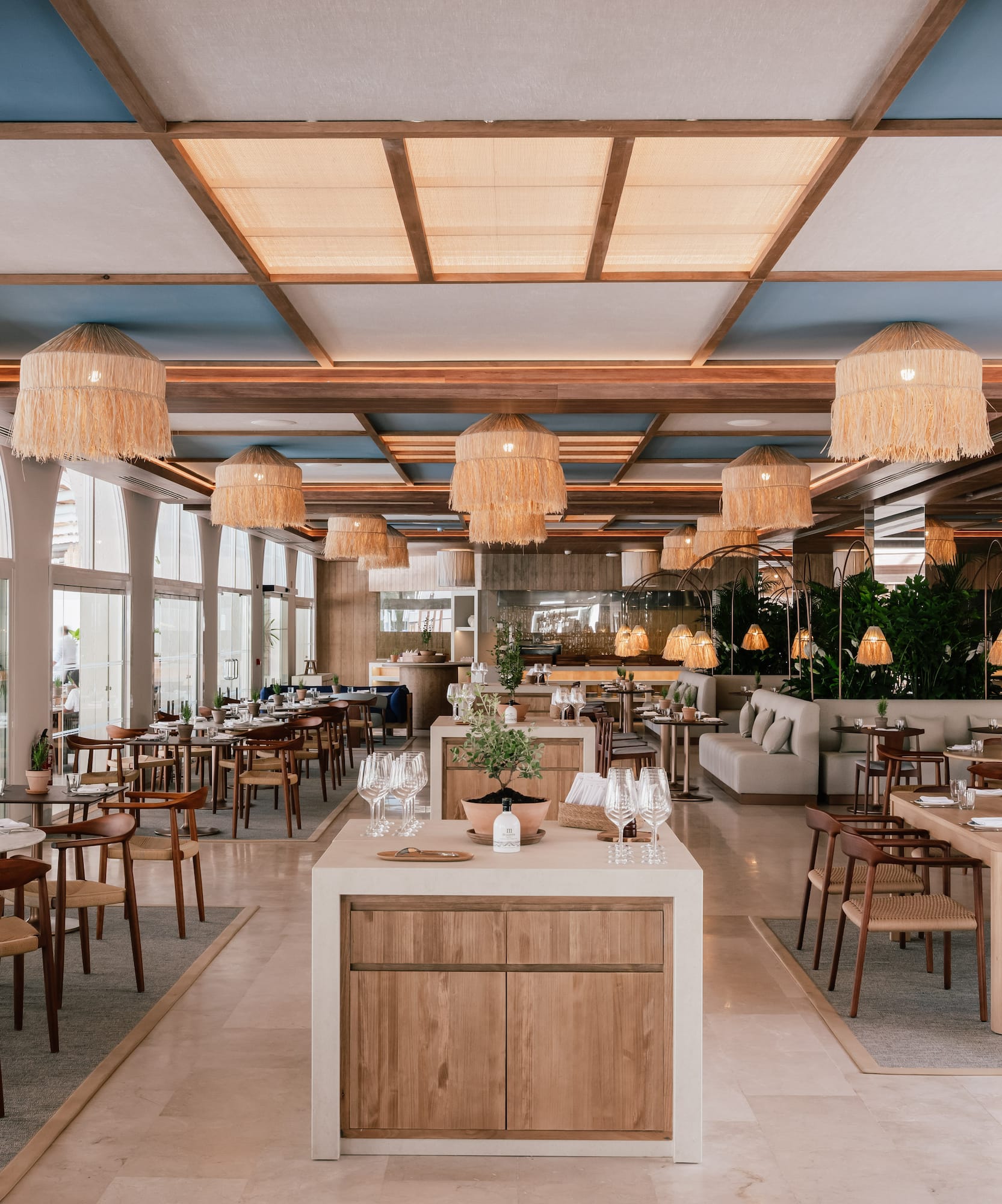 Modern restaurant dining room with wood tables, rattan lights, blue ceiling.