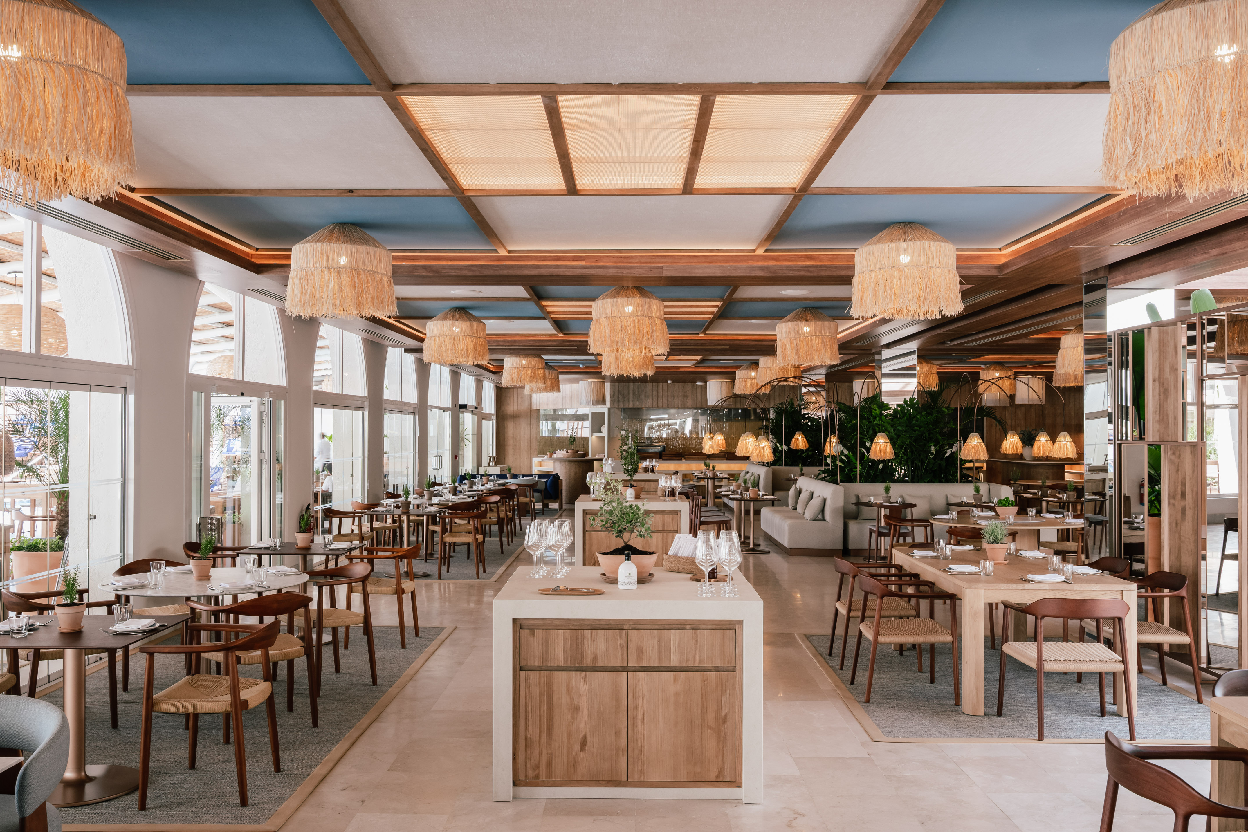 Modern restaurant dining room with wood tables, rattan lights, blue ceiling.