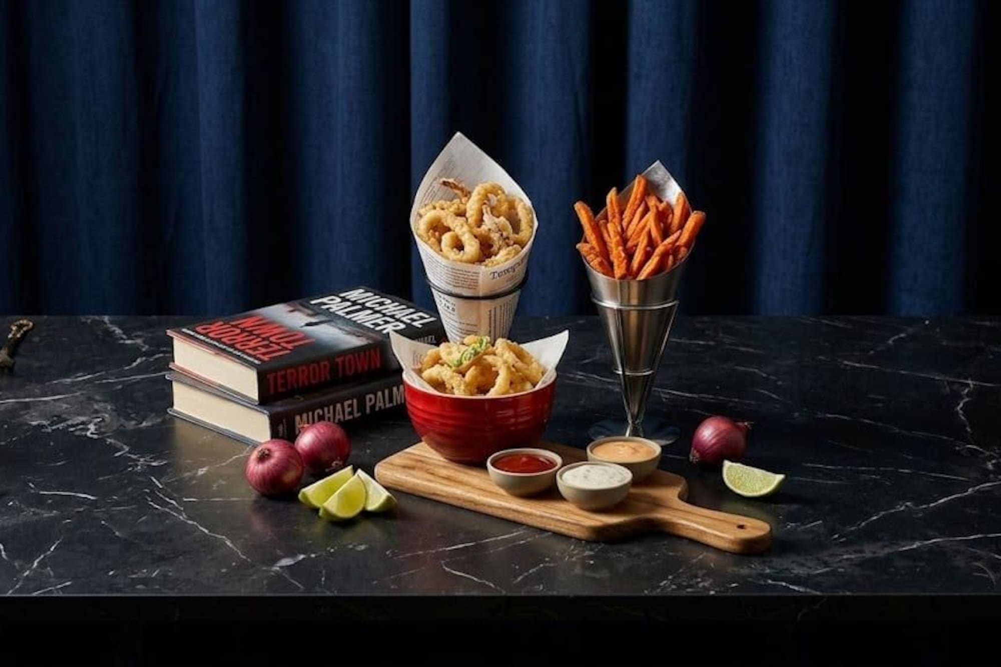 Calamari, sweet potato fries, sauces, and books on a dark marble table.