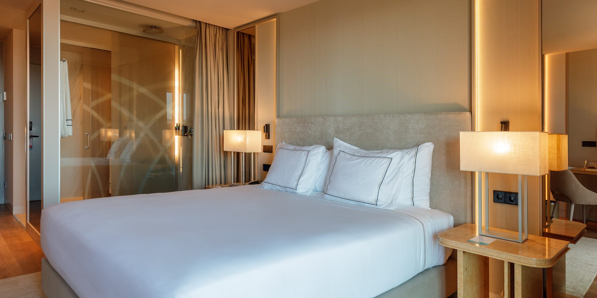 a bed with white sheets and a lamp next to a glass door