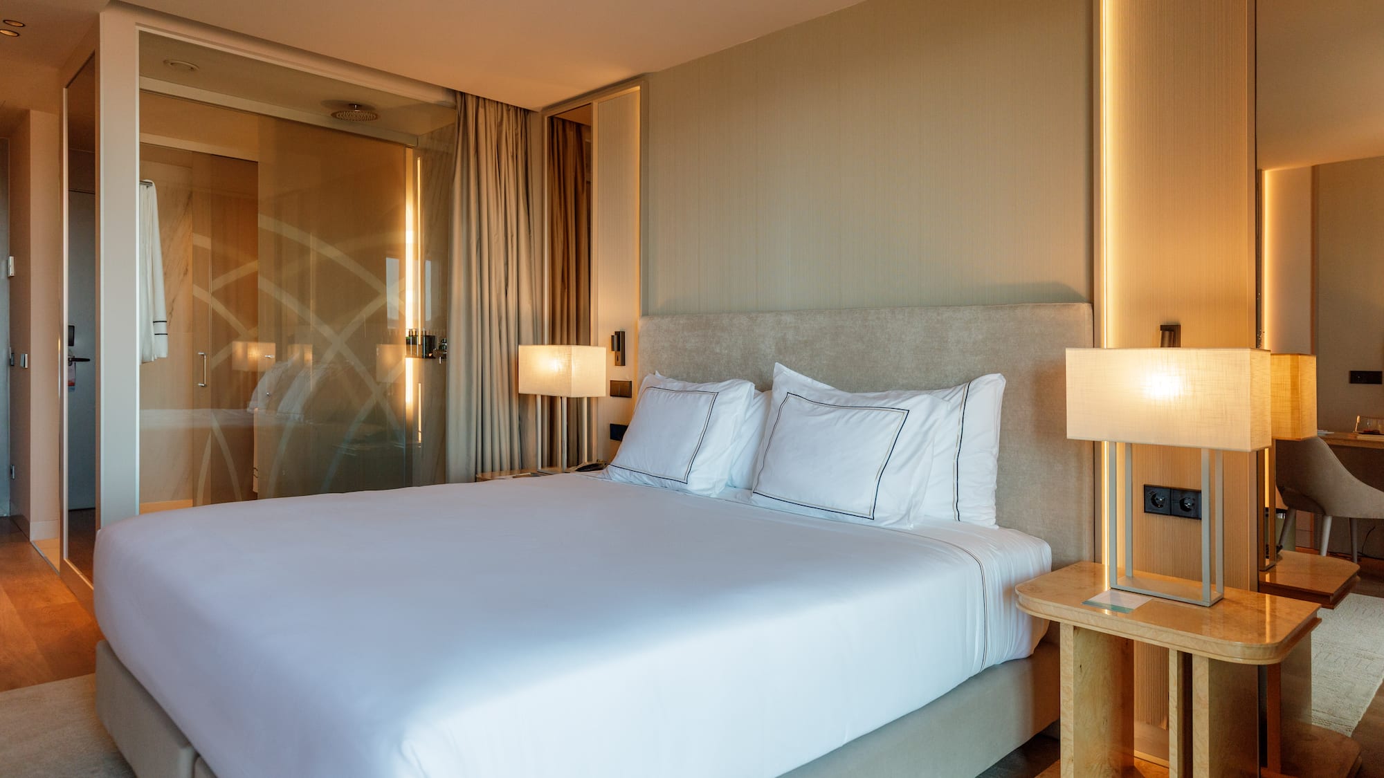 a bed with white sheets and a lamp next to a glass door