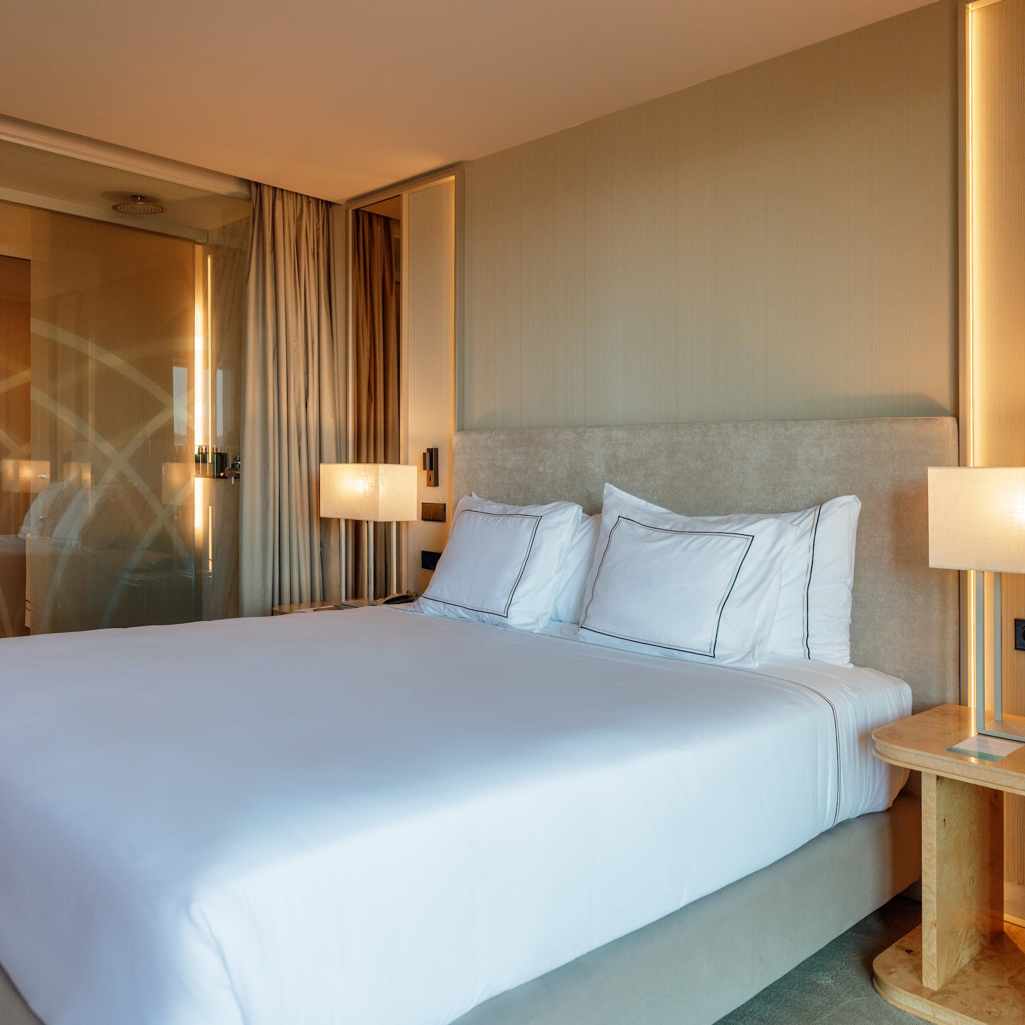 a bed with white sheets and a lamp next to a glass door