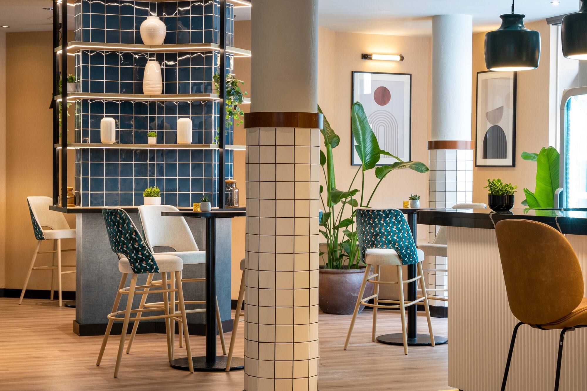 Modern bar lounge interior with blue tiled wall, stylish high stools, plants, and art.