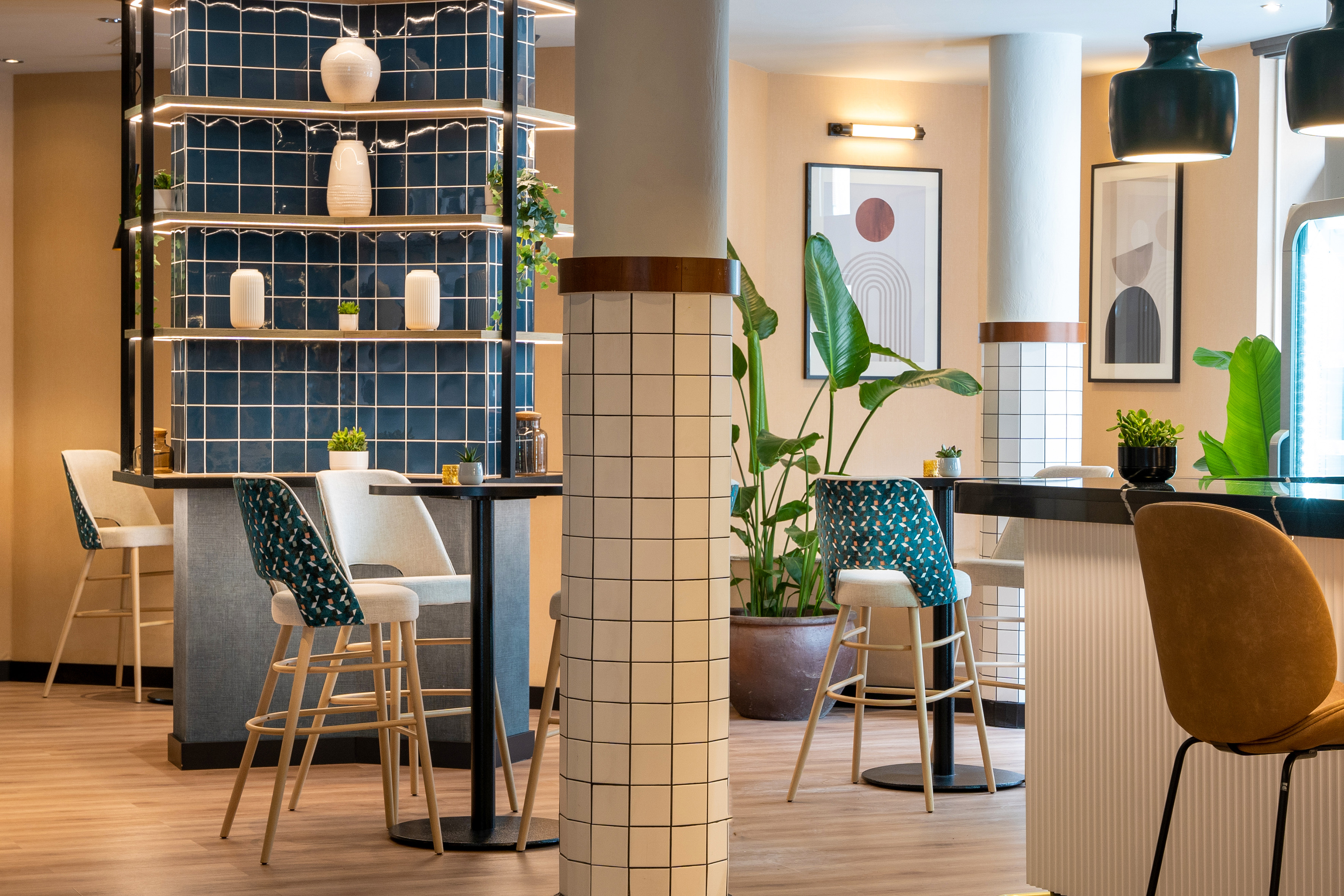 Modern bar lounge interior with blue tiled wall, stylish high stools, plants, and art.
