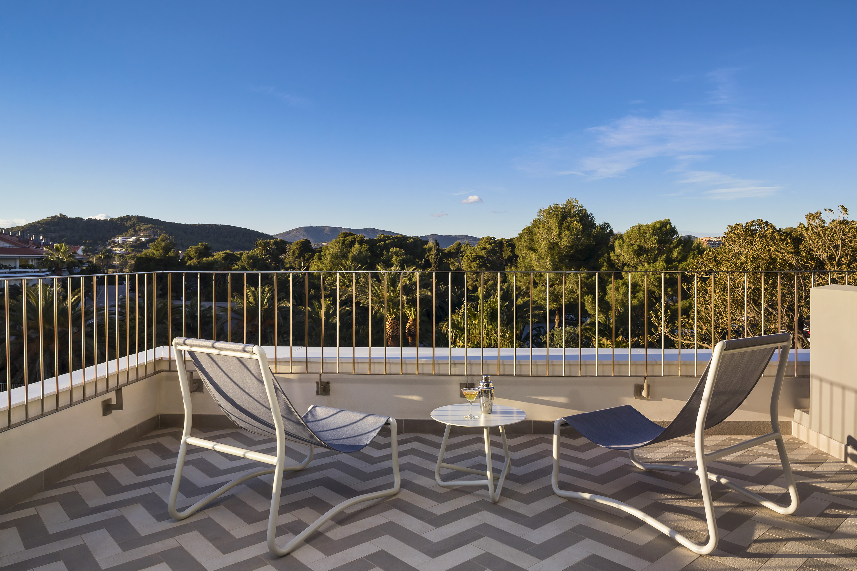Scenic resort balcony with lounge chairs, cocktail, and lush mountain view.