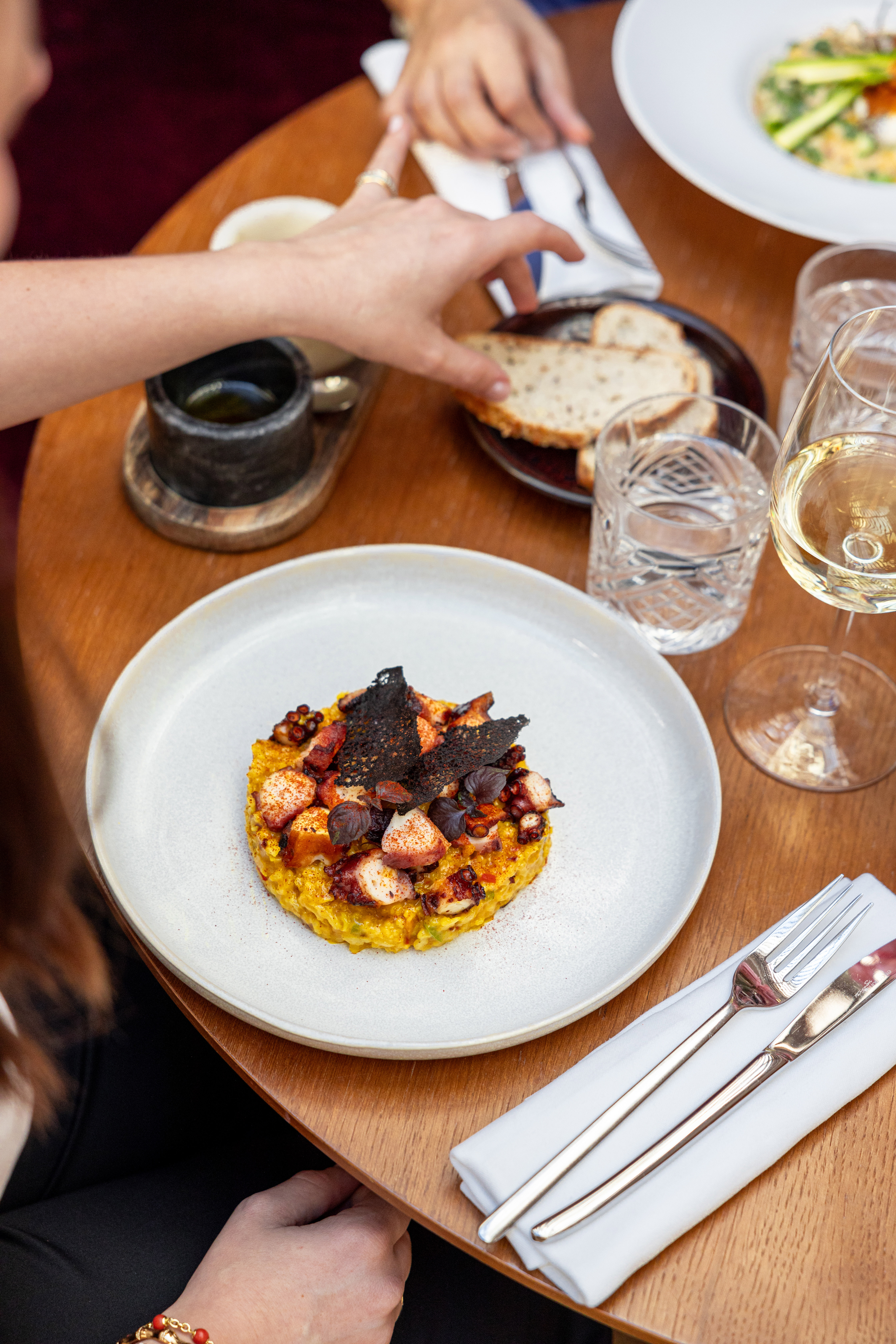 Grilled octopus and saffron risotto with black crisps on a restaurant table.