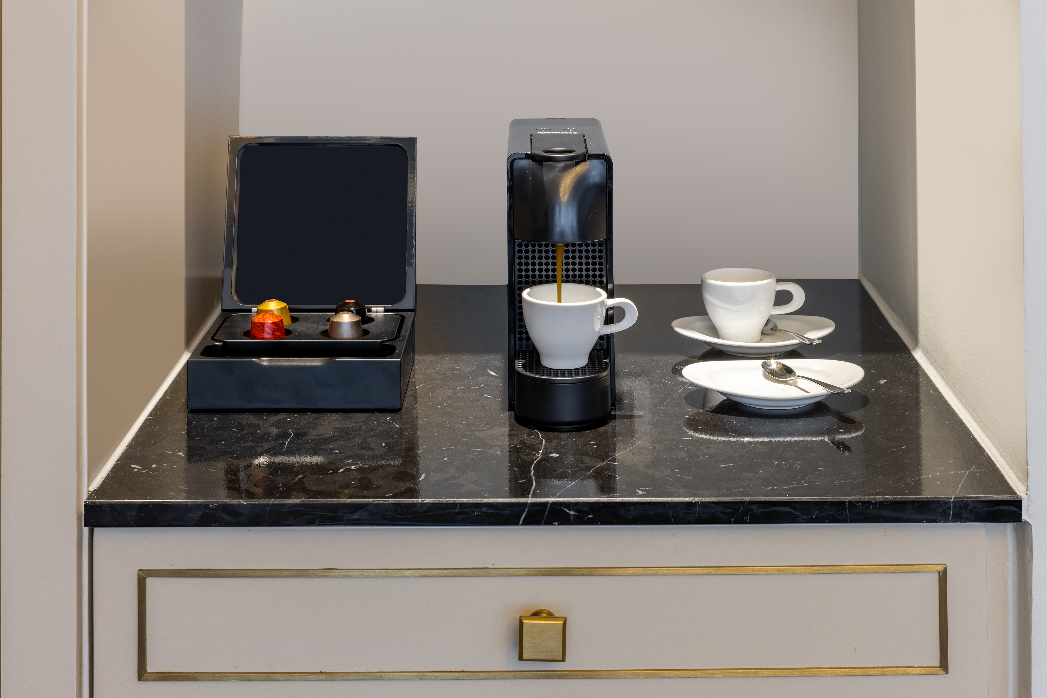 Nespresso machine brewing coffee into a white cup on a black marble counter.