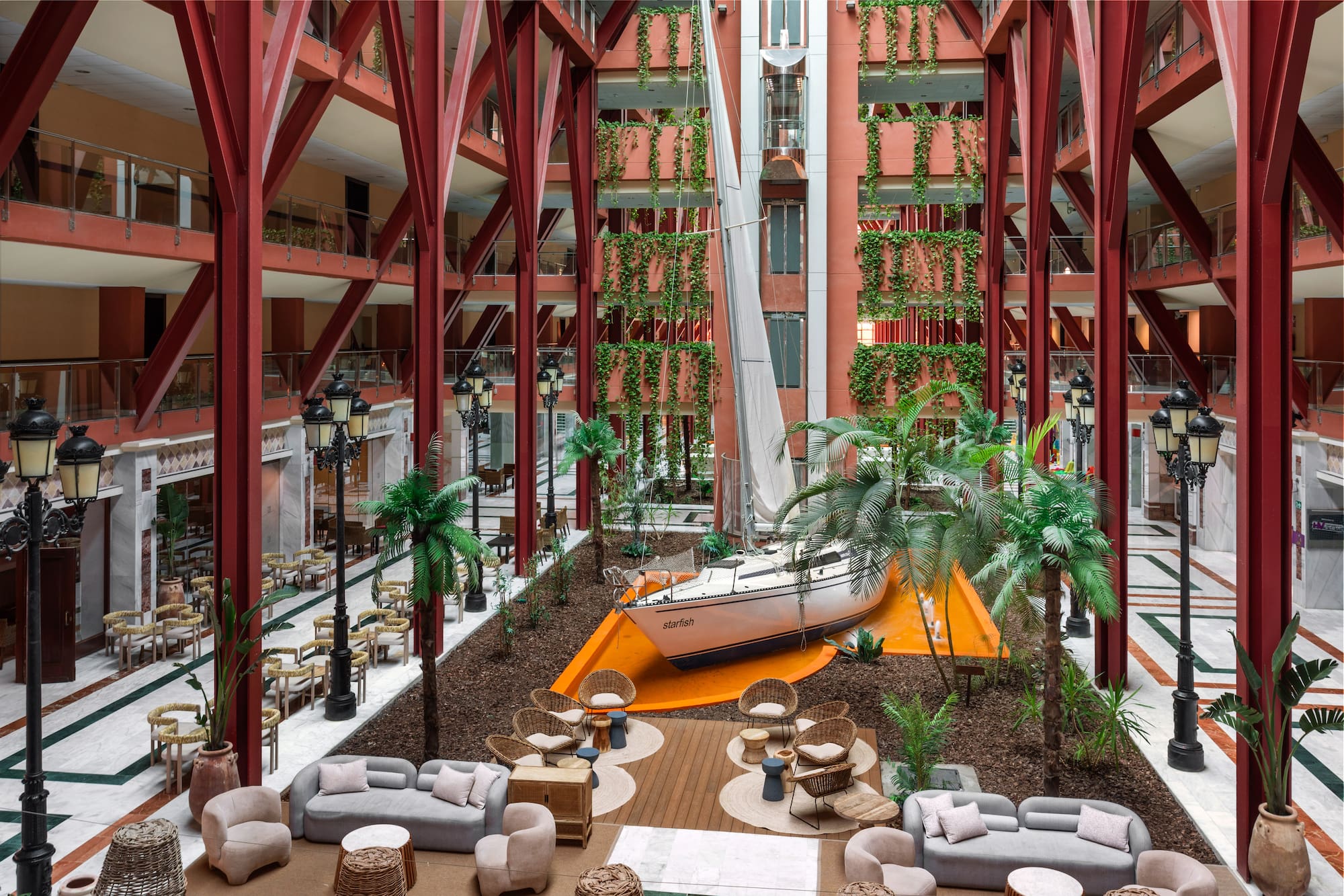 Hotel atrium with large sailboat, red structural beams, vertical gardens, and lounge.