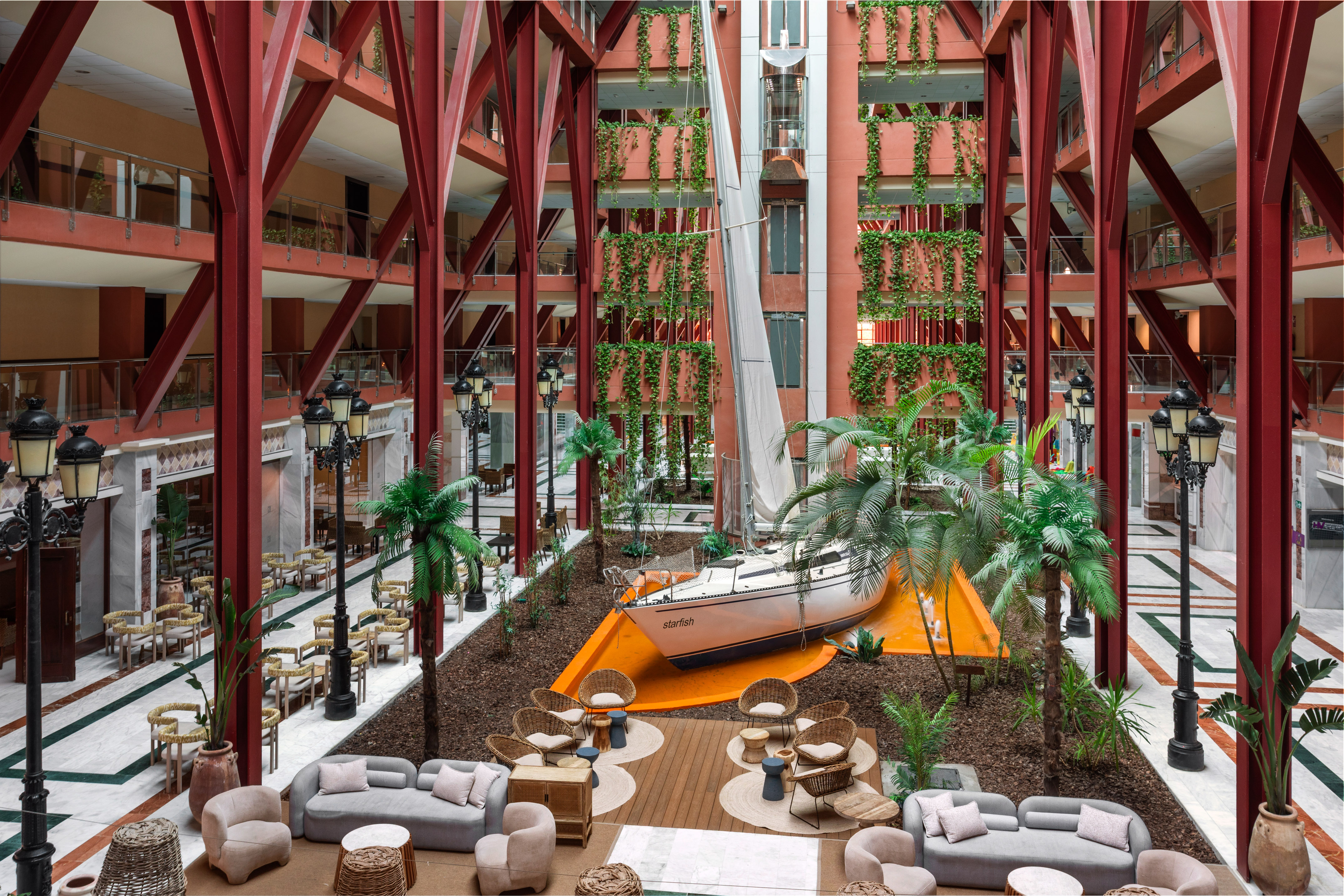 Hotel atrium with large sailboat, red structural beams, vertical gardens, and lounge.