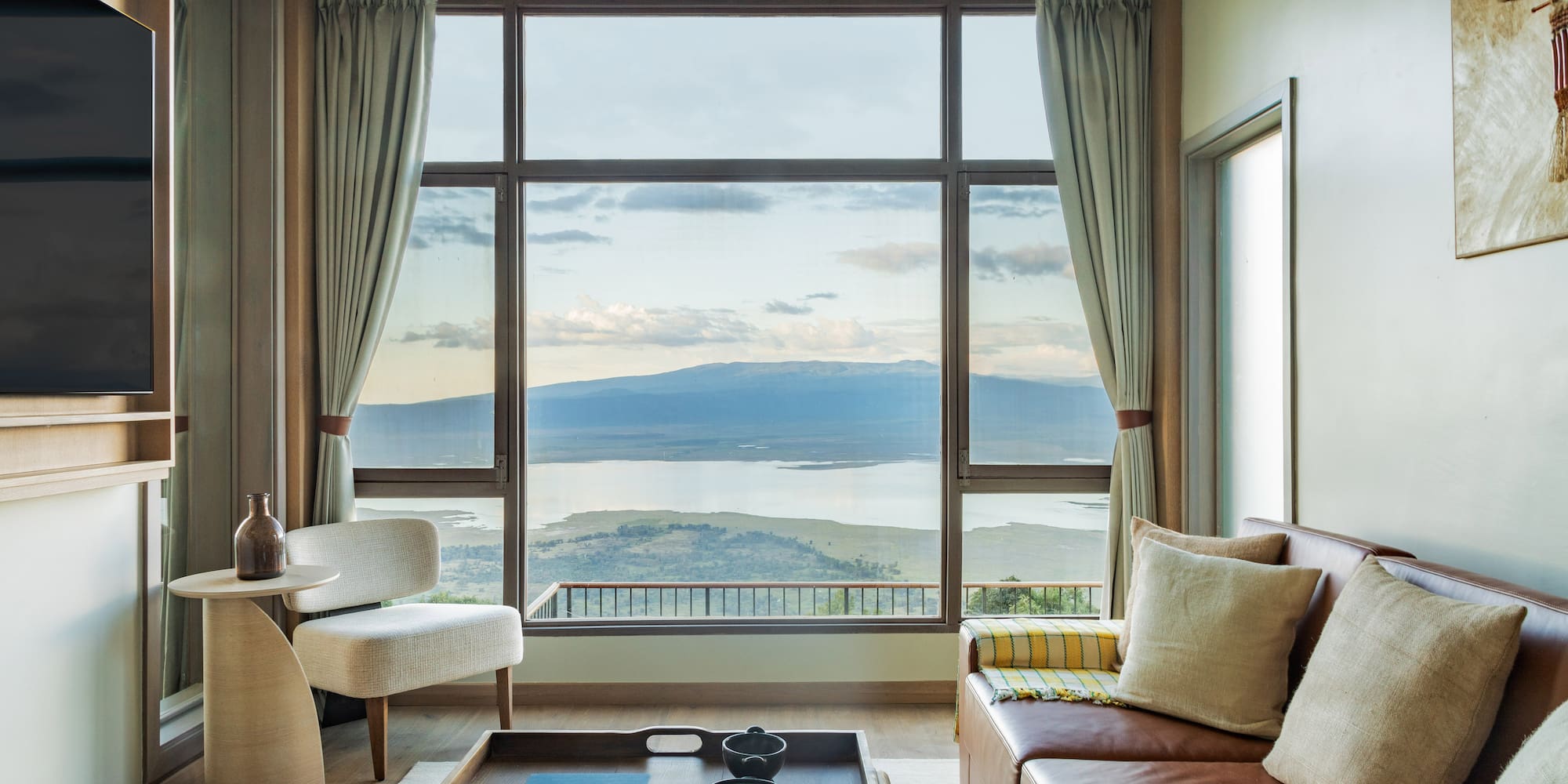 Safari lodge lounge with large window, scenic lake and mountain views.