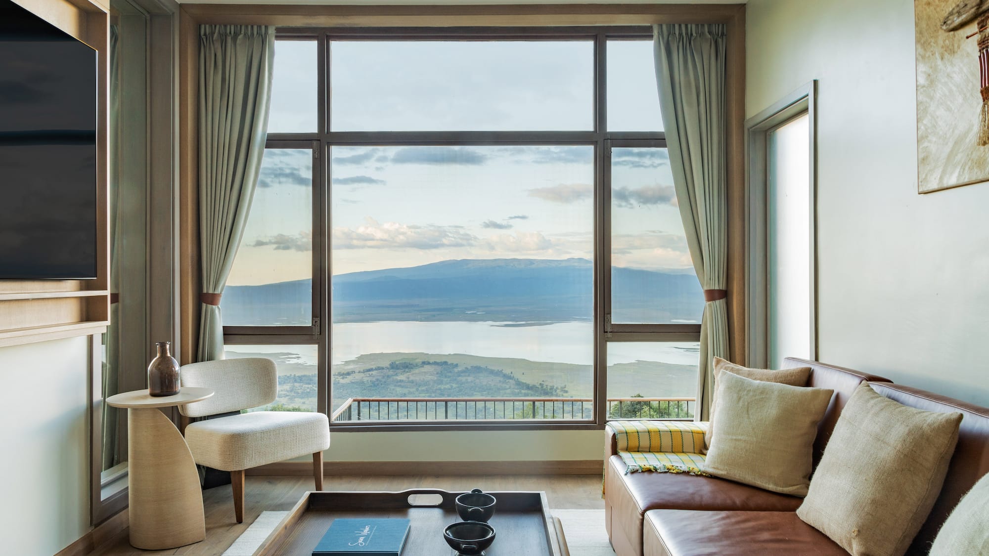Safari lodge lounge with large window, scenic lake and mountain views.