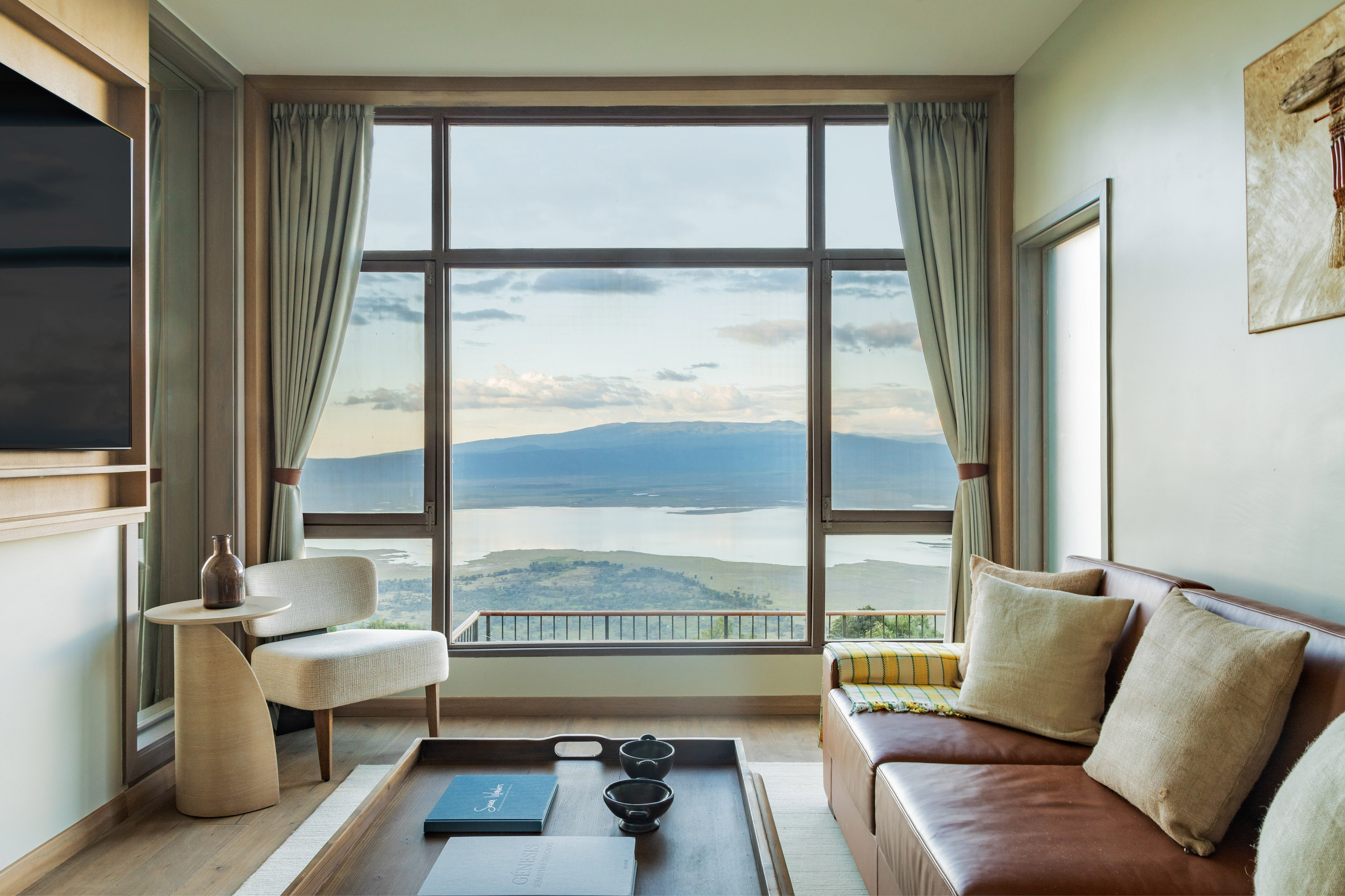 Safari lodge lounge with large window, scenic lake and mountain views.