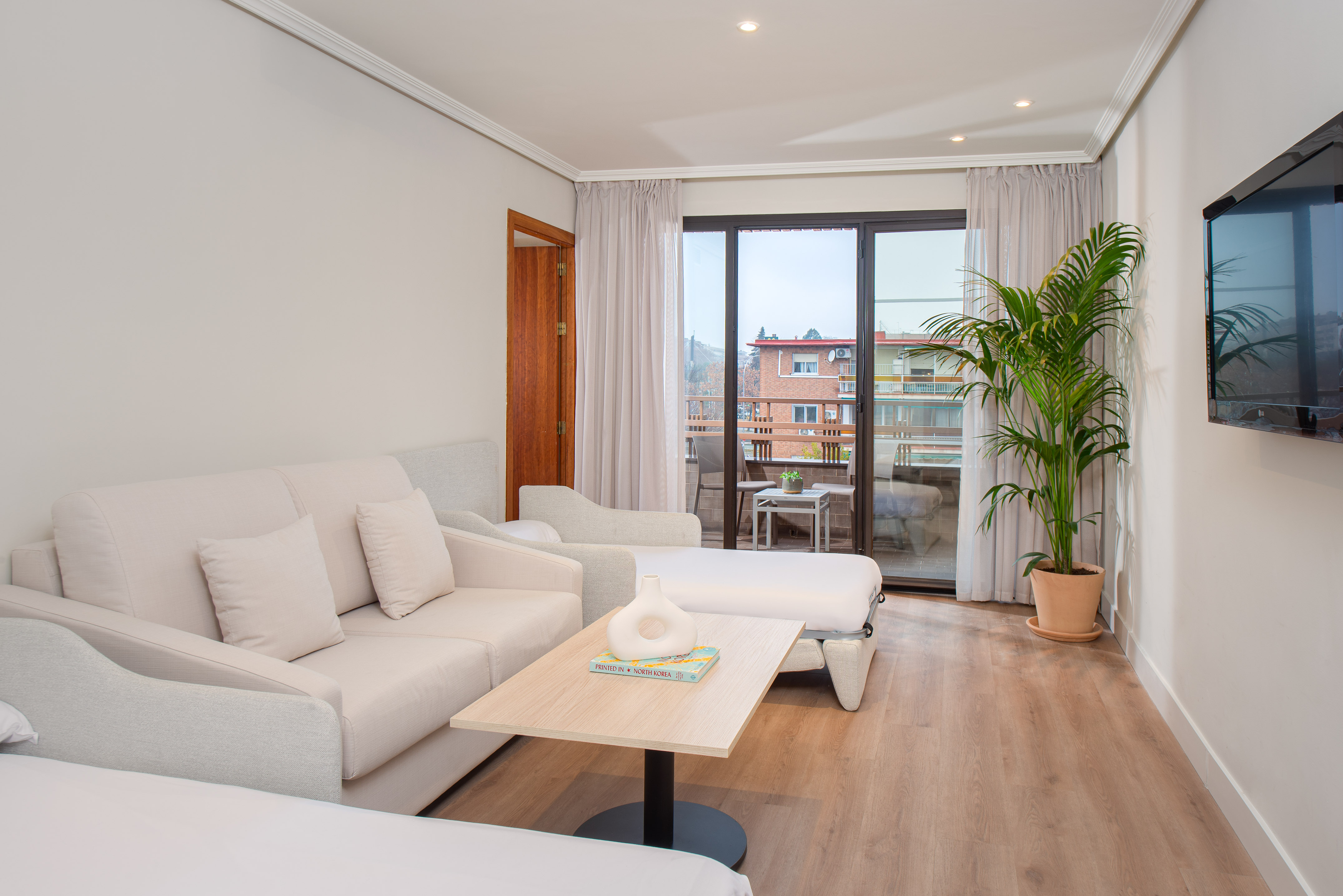 Modern hotel suite living room with sofa, wood floor, balcony, and plant.
