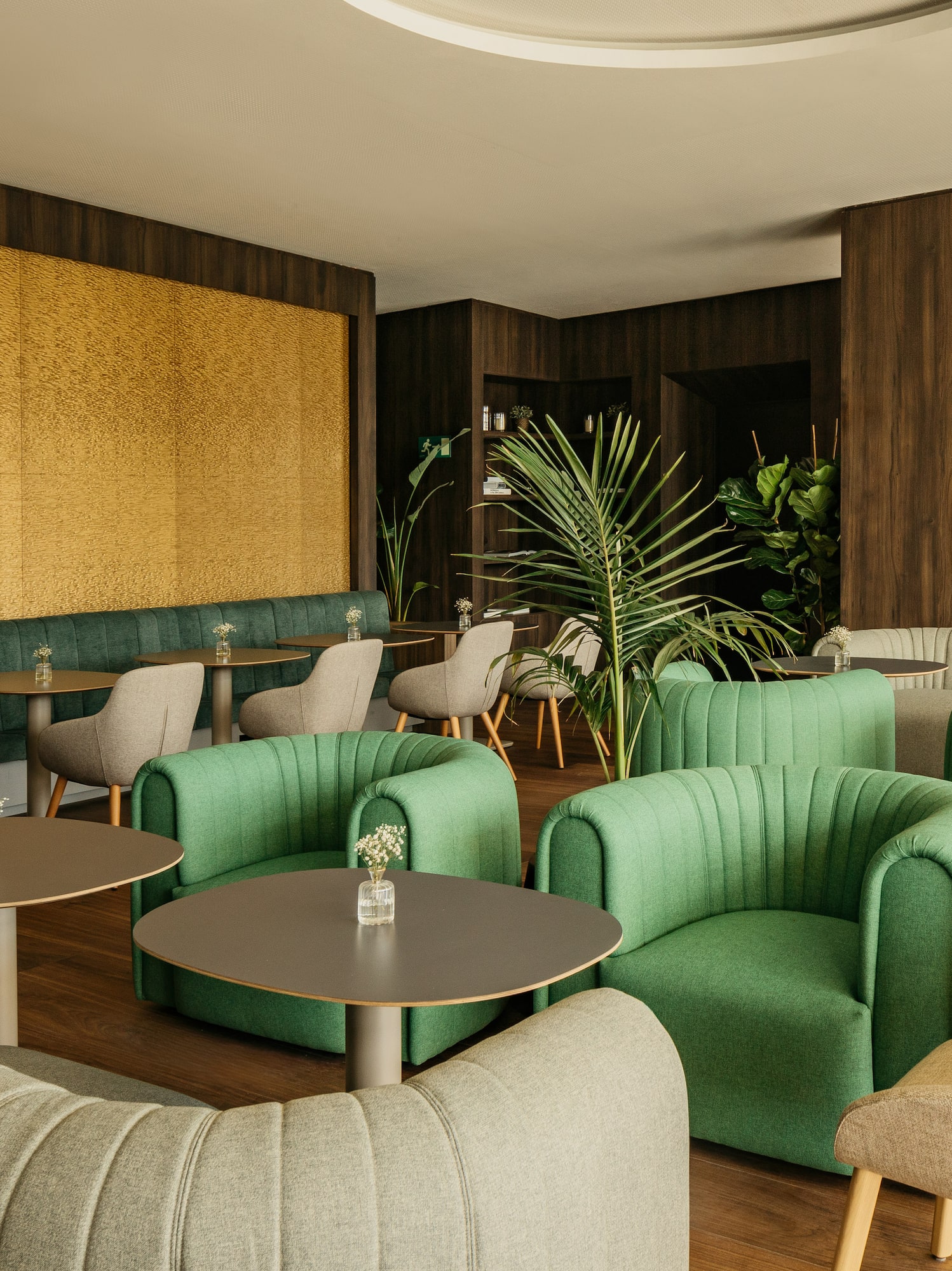Modern lounge interior with green chairs, gold wall, dark wood, and plants.