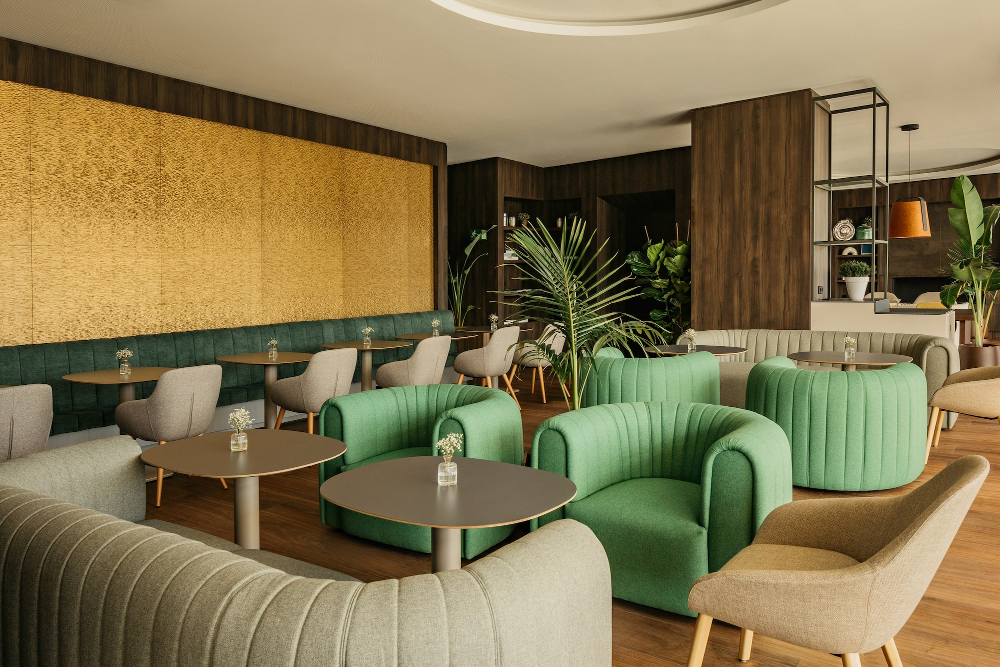Modern cafe lounge with green seating, wood tables, yellow wall, and plants.