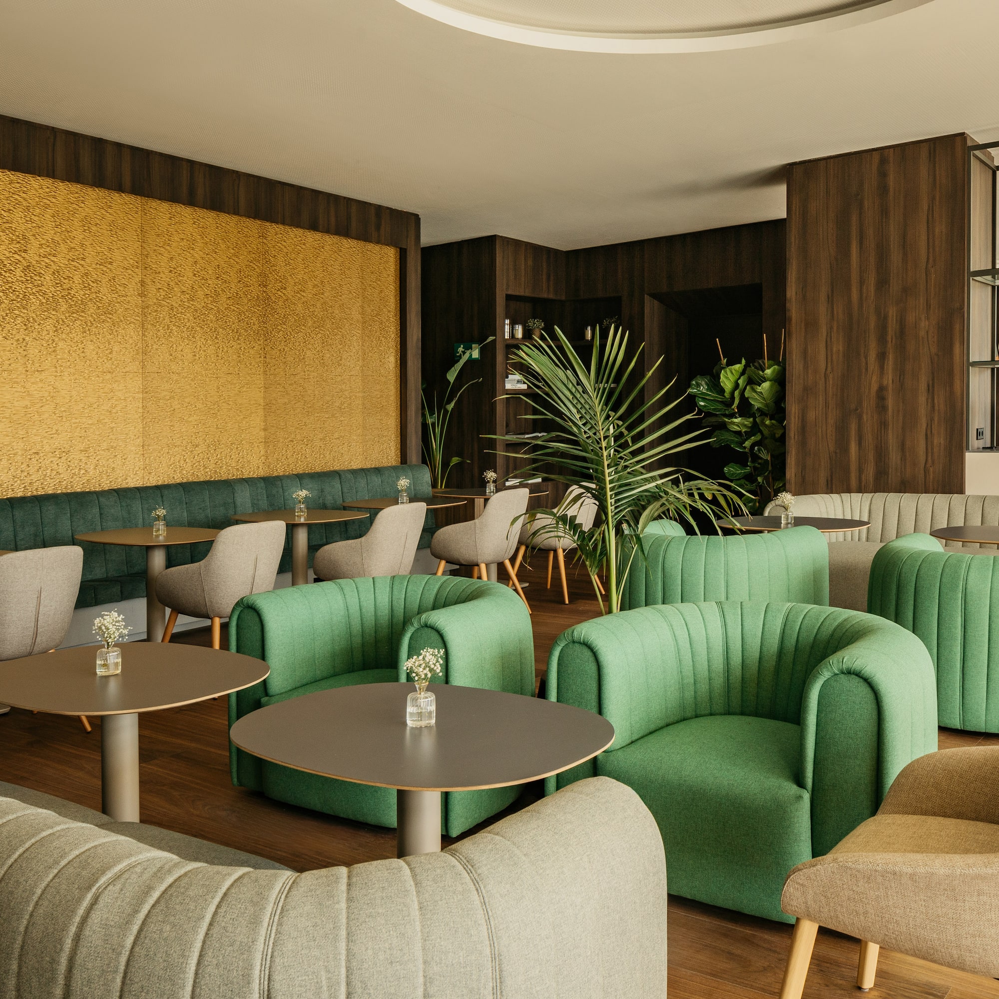 Modern cafe lounge with green seating, wood tables, yellow wall, and plants.