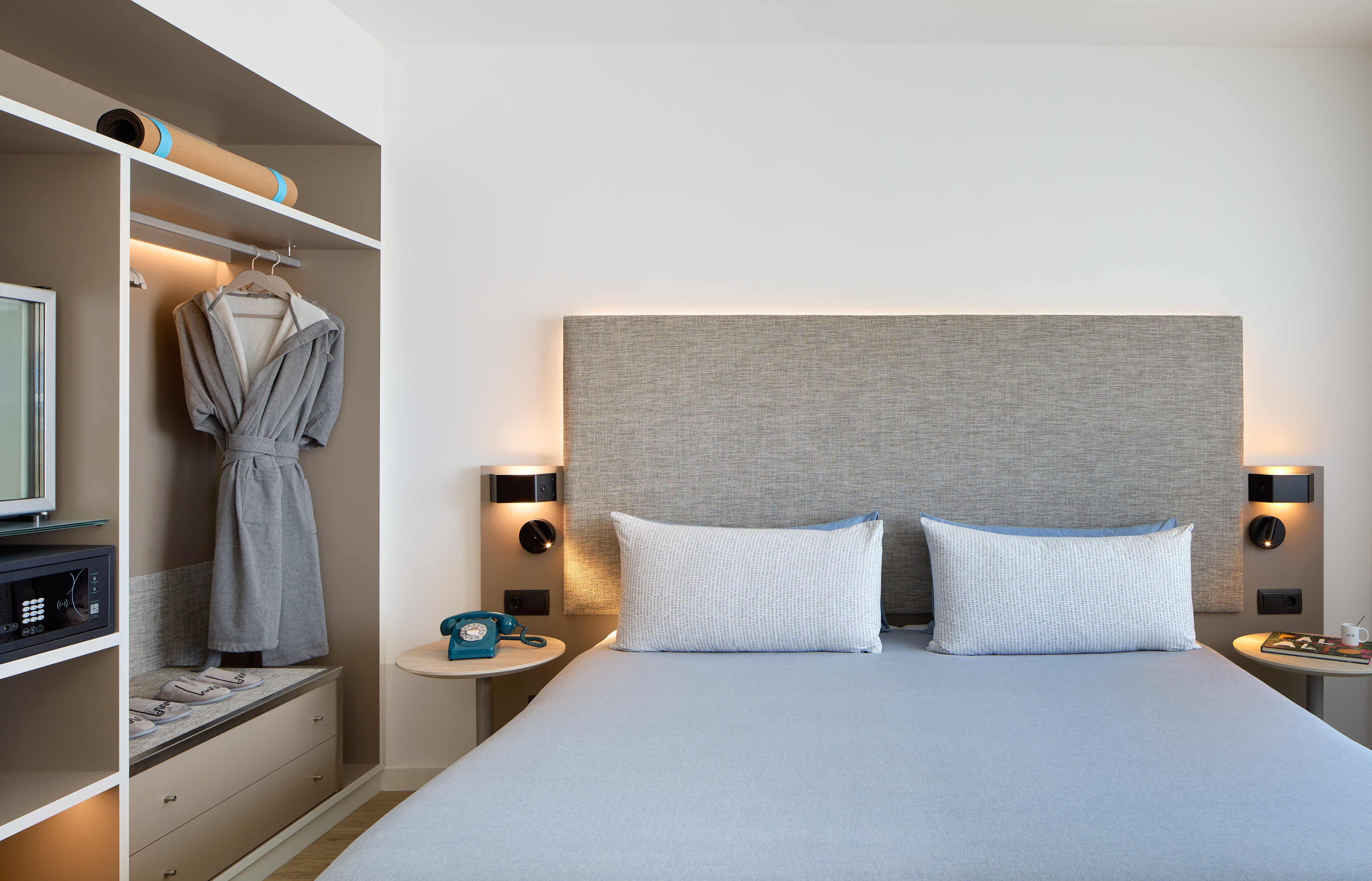 Hotel room with bed, fabric headboard, open wardrobe, bathrobe, and yoga mat.