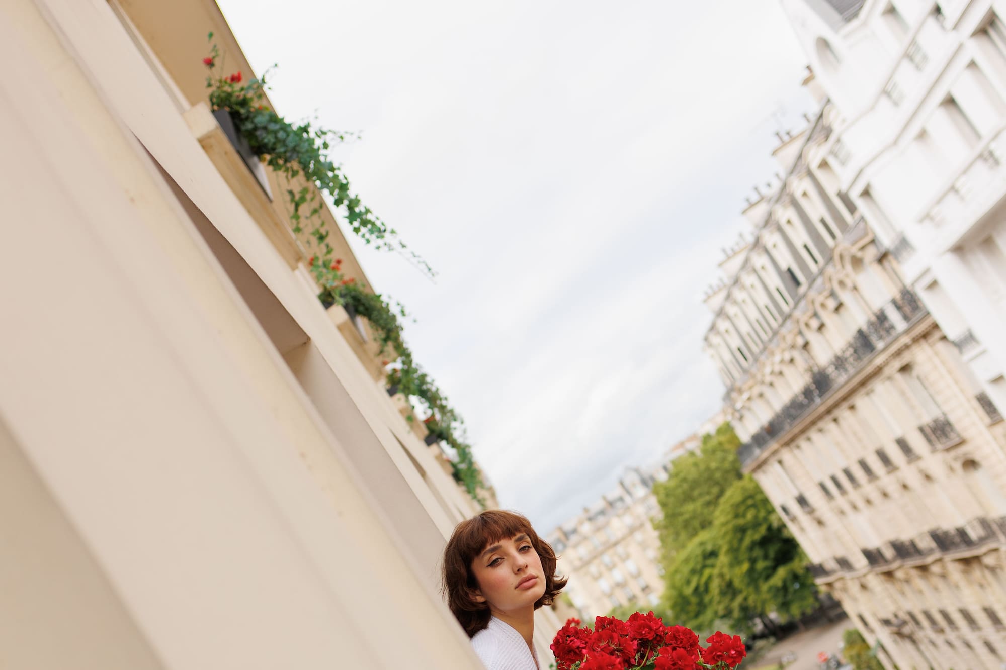 Mujer en balcón con flores rojas, vista urbana de París.