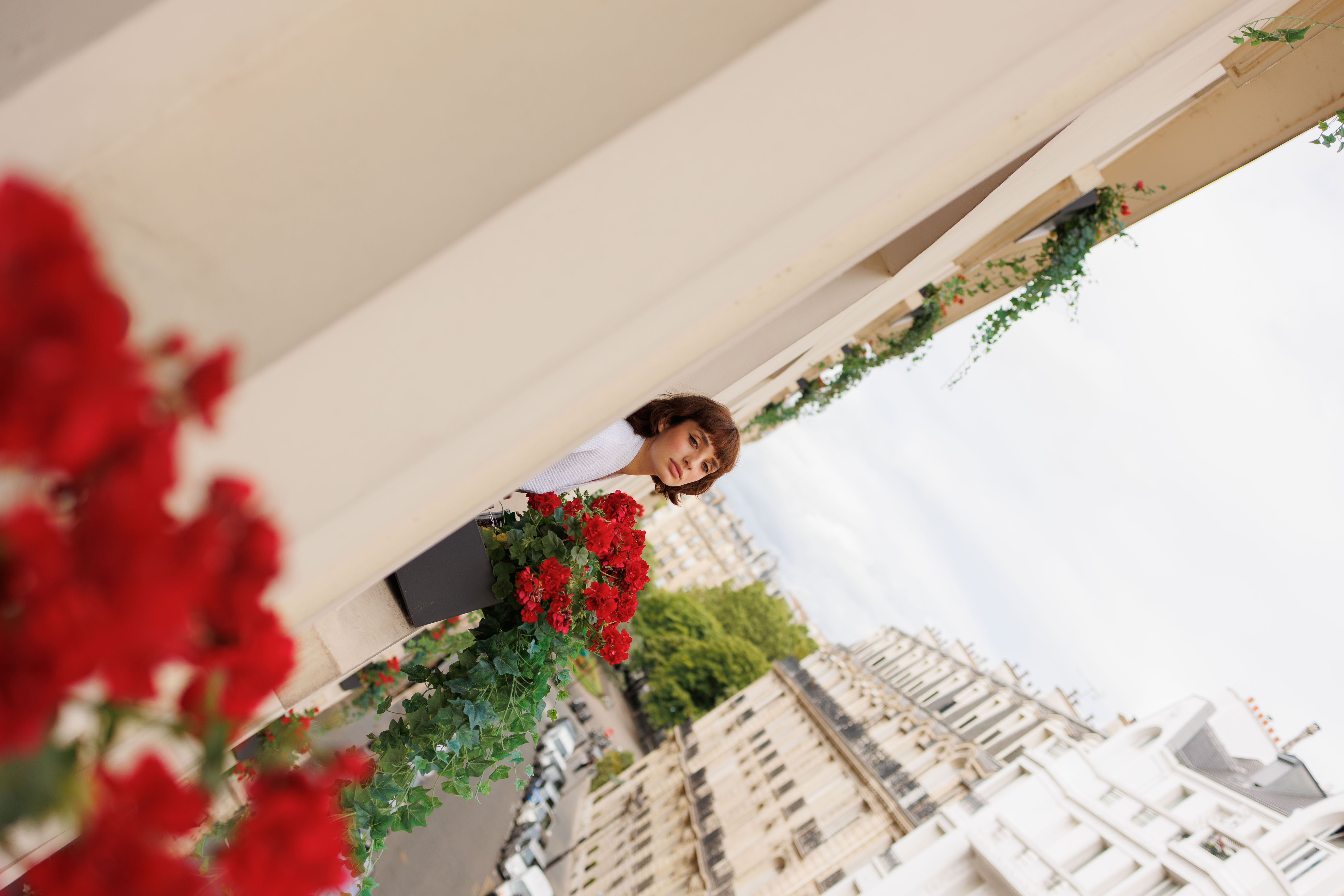 Mujer en balcón con flores rojas, vista urbana de París.