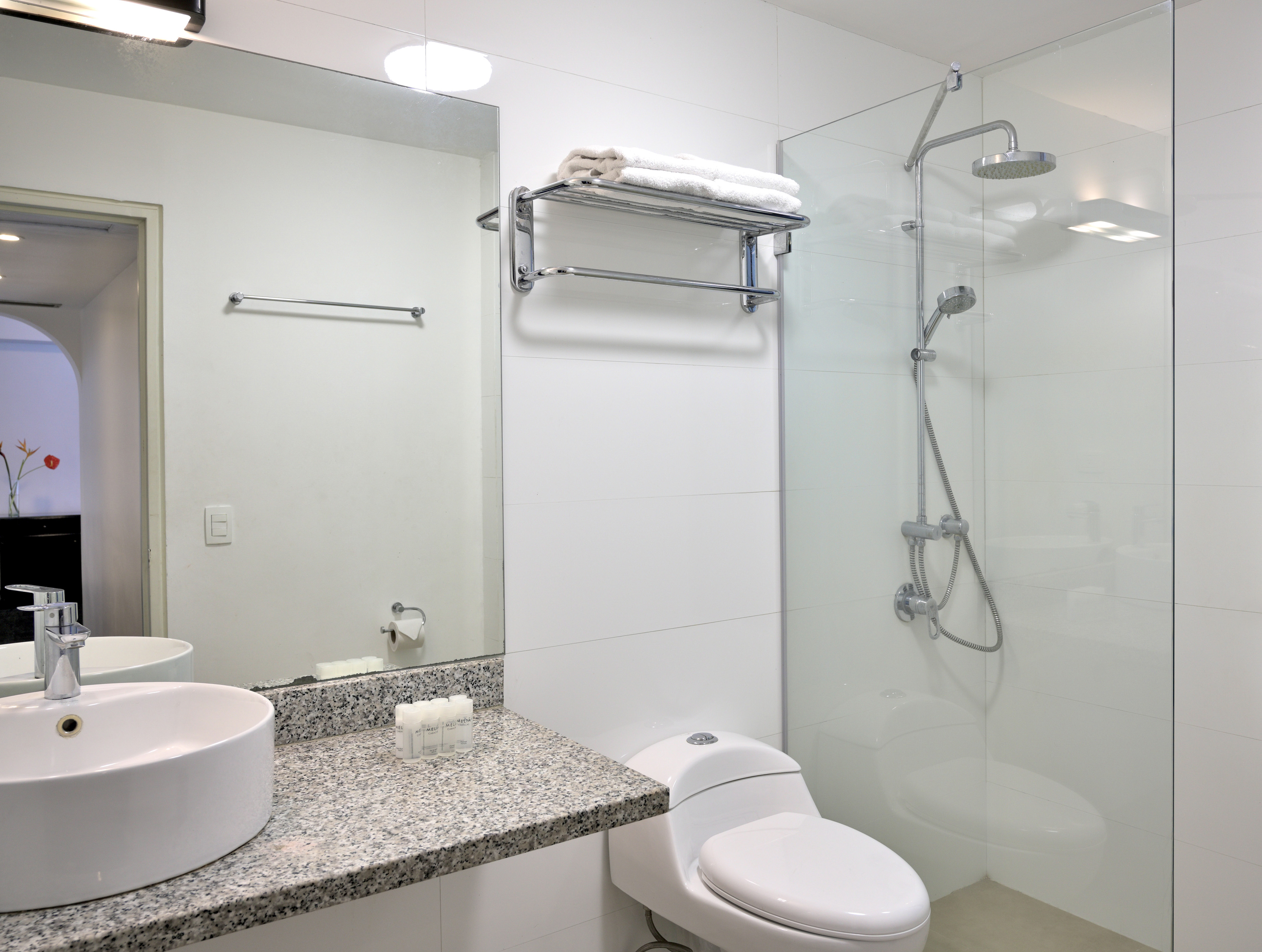 Modern white bathroom: glass shower, toilet, sink, granite counter.