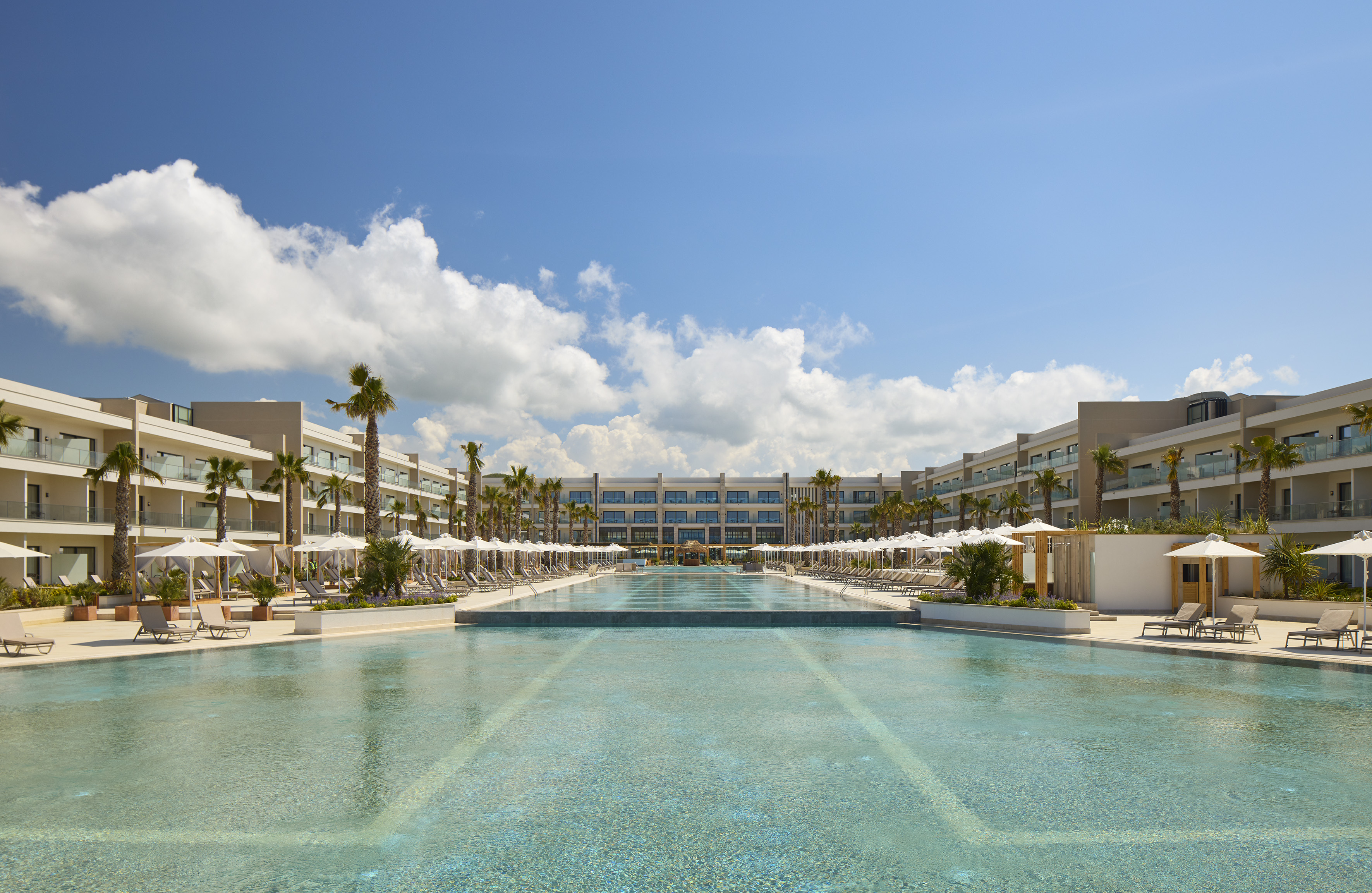 a pool with umbrellas and palm trees in front of a hotel